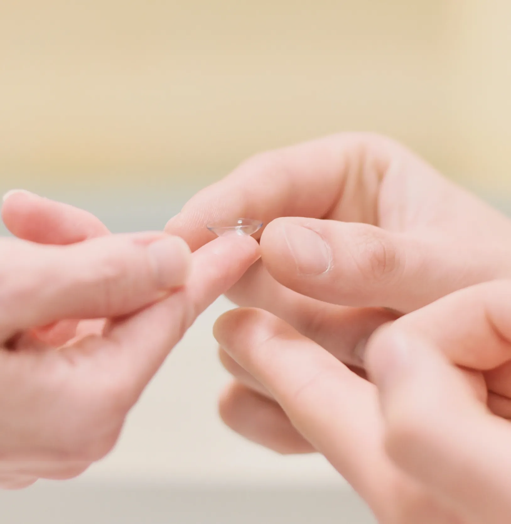 Hände halten eine klare Kontaktlinse auf einem Finger.