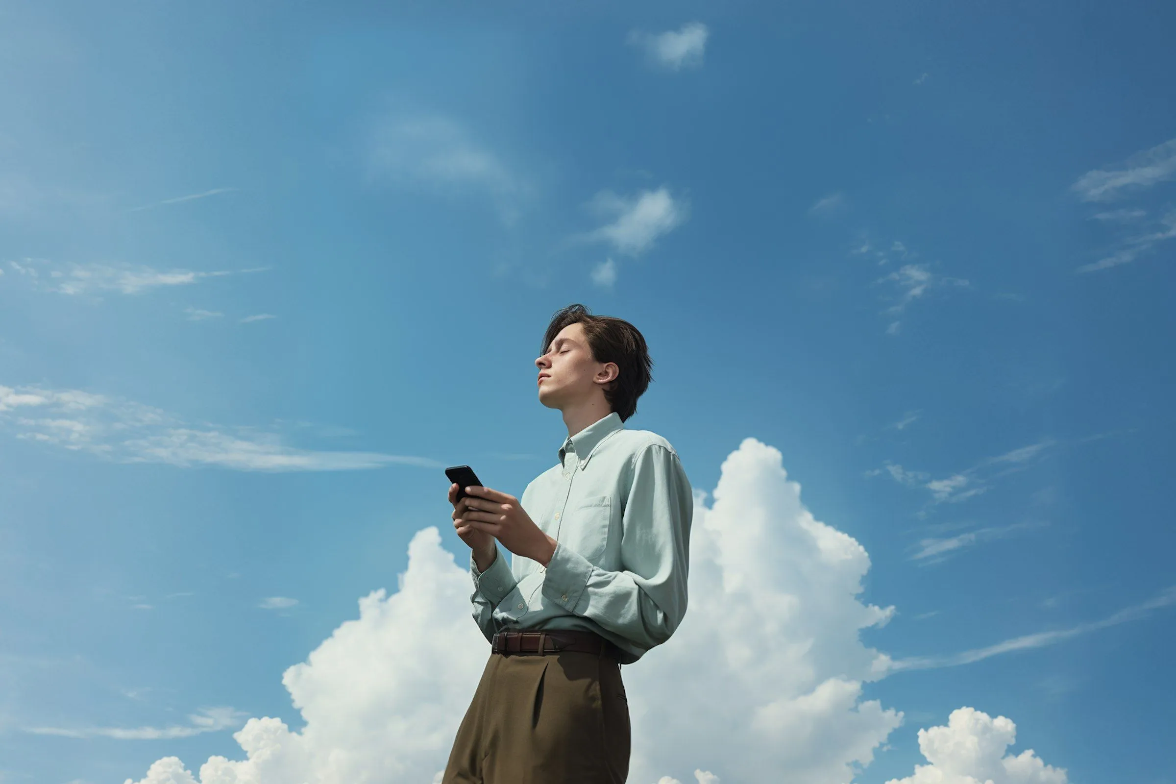 A man standing in front of a blue sky holding a cell phone.