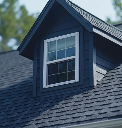 Close-up of a blue dormer window with white trim on a gray shingled roof under daylight.
