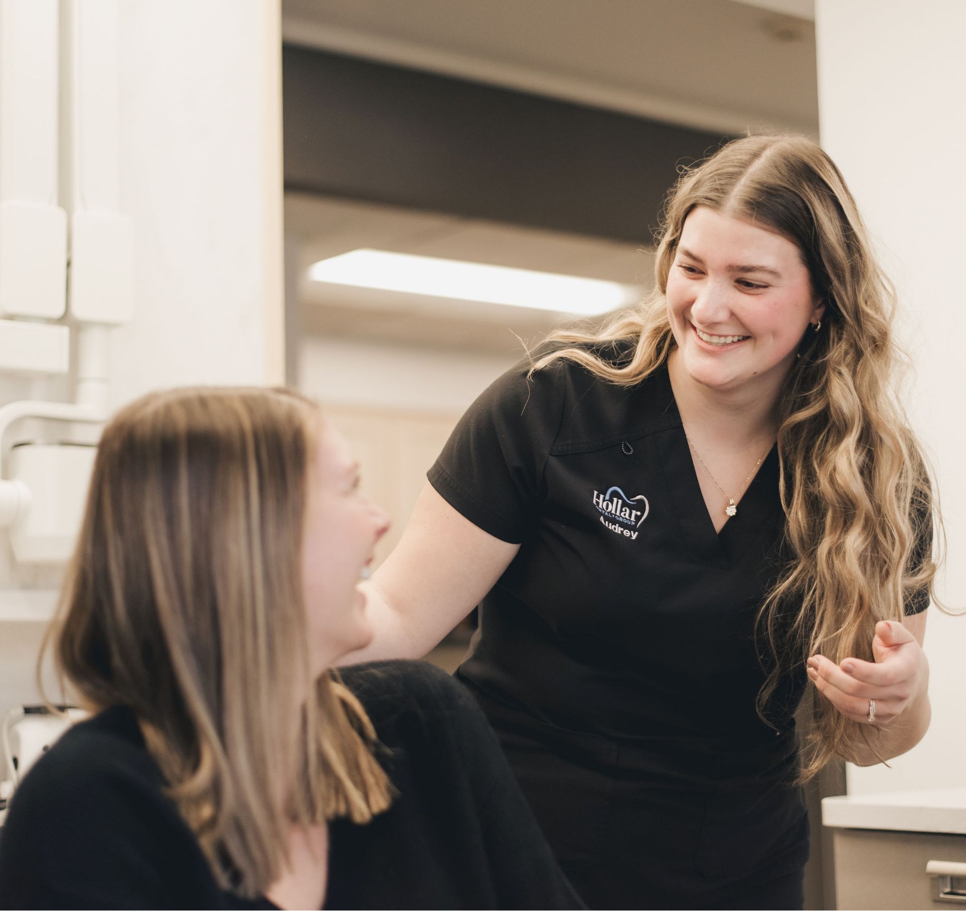 Female dental professional smiling and interacting with a female patient in a dental office.