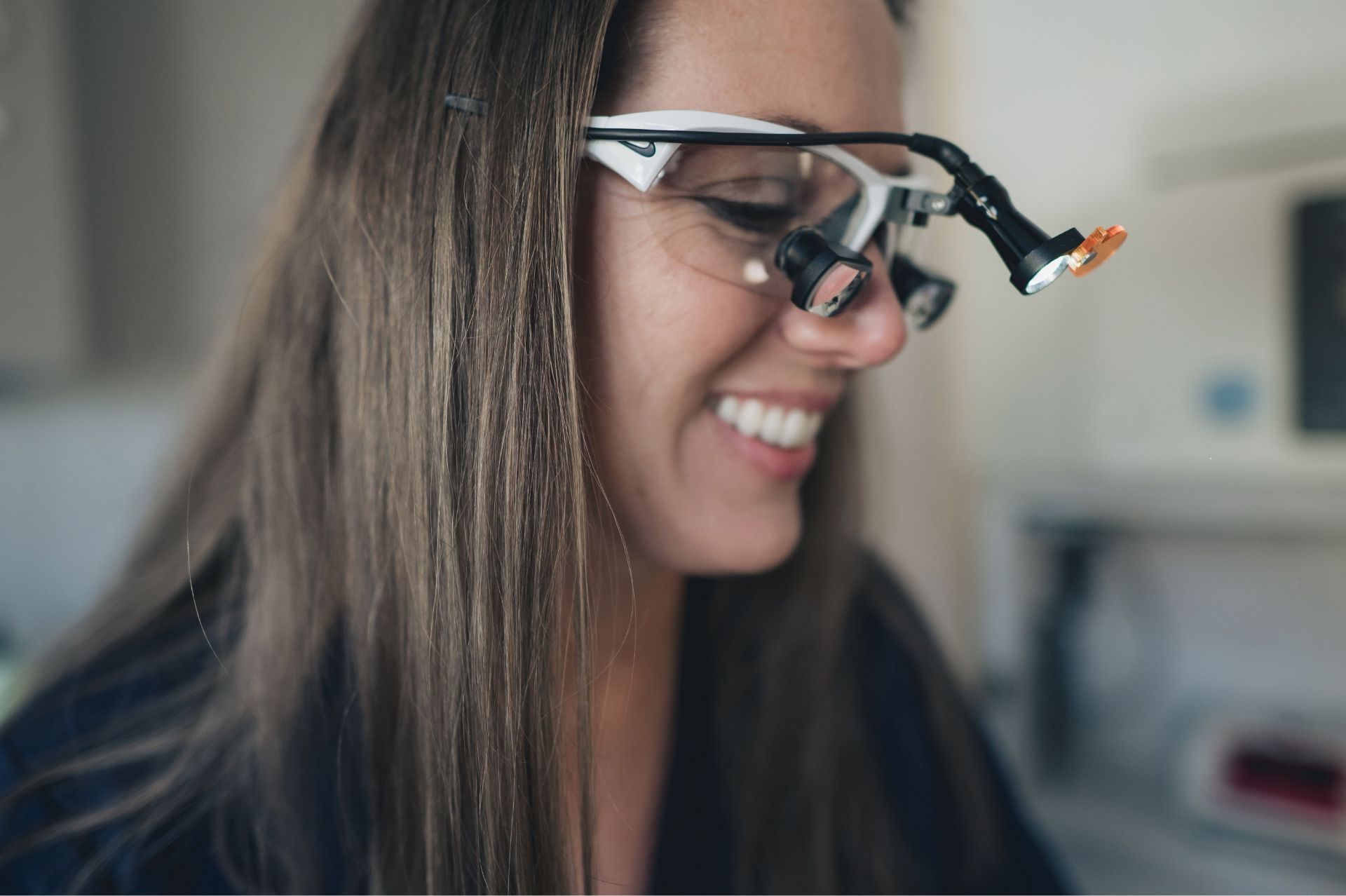Smiling woman wearing magnifying glasses with an attached light, looking down.