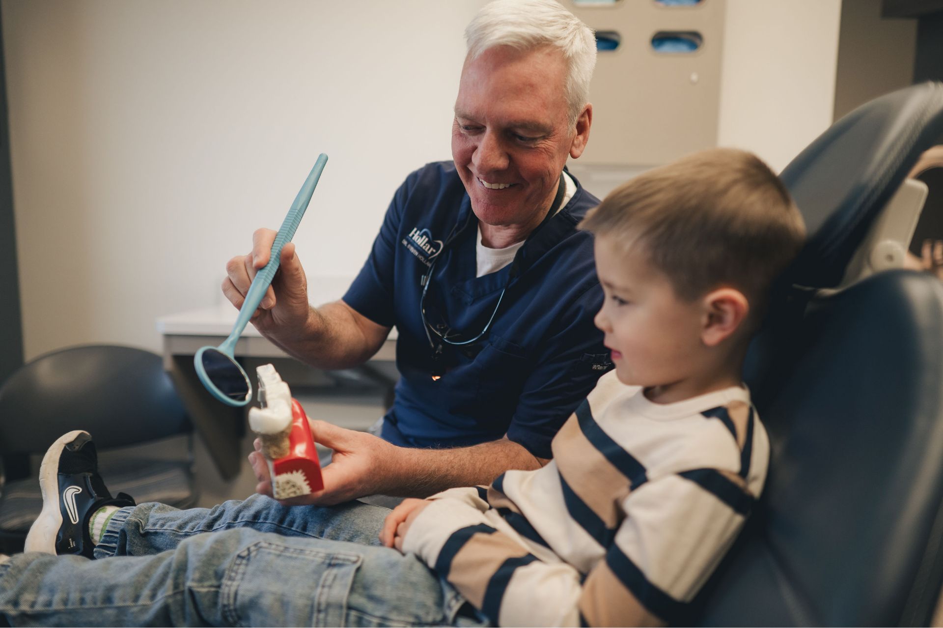 Dentist showing a dental model to a young boy sitting in a dental chair.