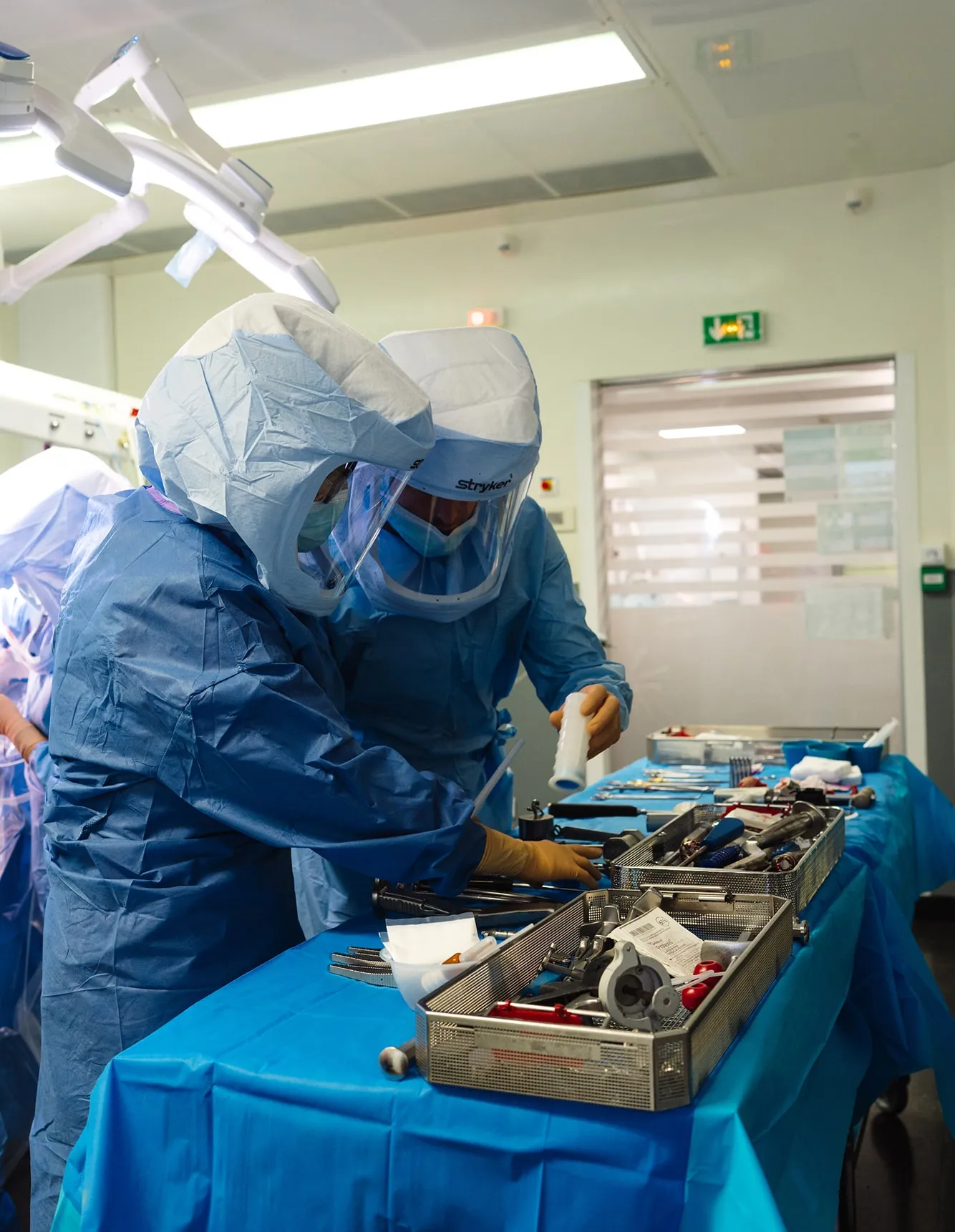 Deux professionnels de la santé en tenue de protection complètes manipulant des instruments chirurgicaux sur une table stérile en salle d'opération.