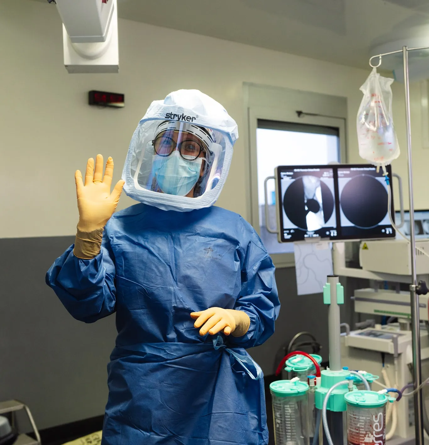 Professionnel de santé en équipement de protection complet souriant et saluant dans une salle d'opération.