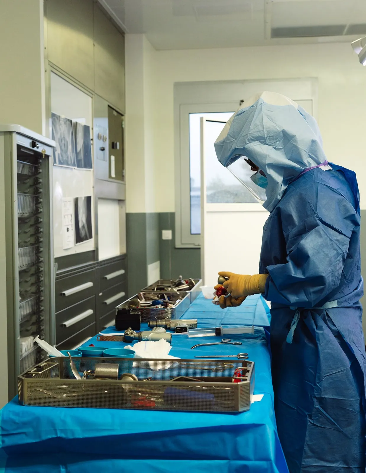 Person en combinaison de protection complète manipulant des instruments chirurgicaux sur une table couverte d'une nappe bleue dans une salle médicale.
