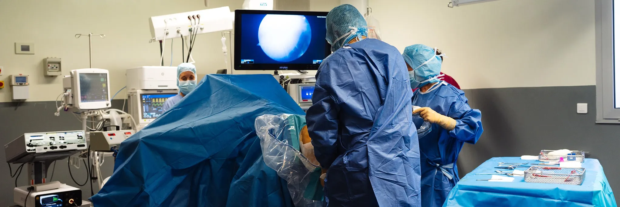 Équipe chirurgicale en tenue complète opérant avec un écran montrant une imagerie médicale dans une salle d'opération.