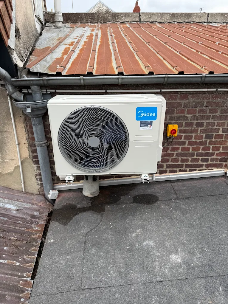 Unité extérieure de pompe à chaleur Midea installée sur un mur en briques sous un toit métallique rouillé.