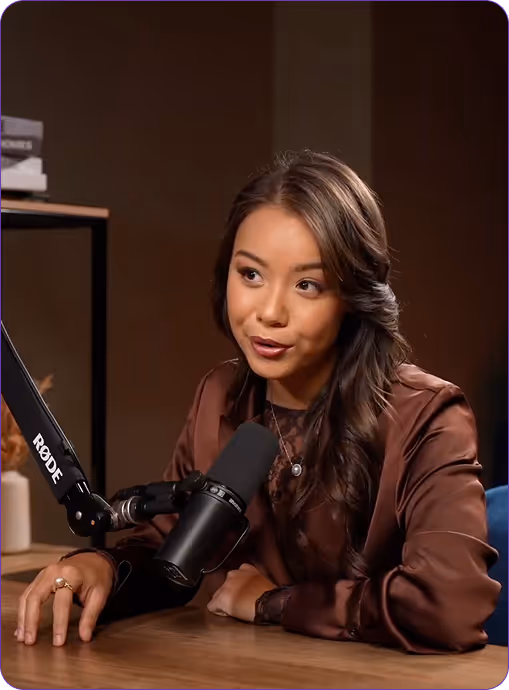 Woman with long dark hair speaking into a Rode microphone at a table in a recording studio.