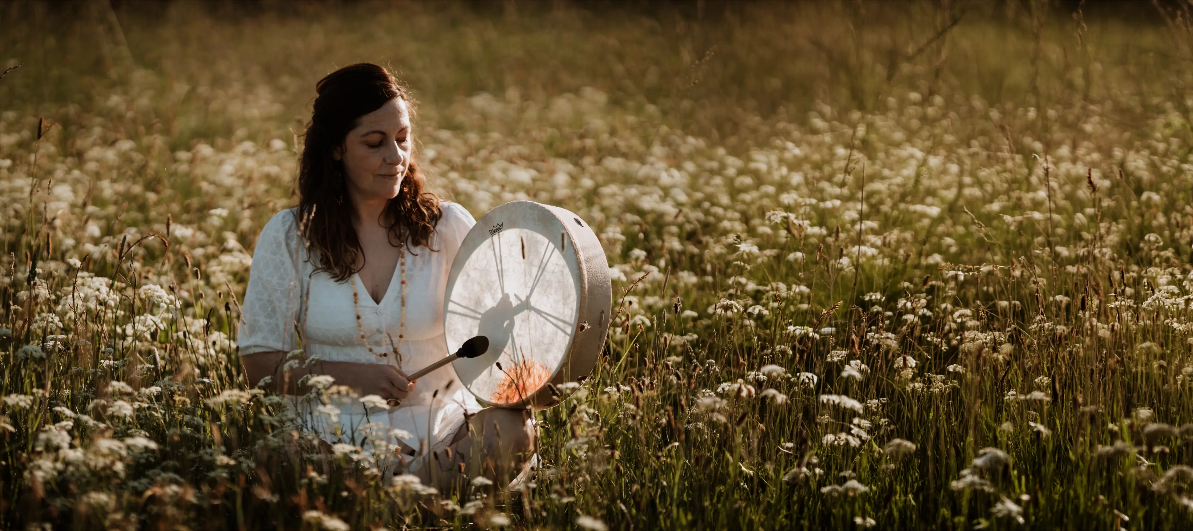 Dawn in white dress sitting in a field of wildflowers playing a drum.