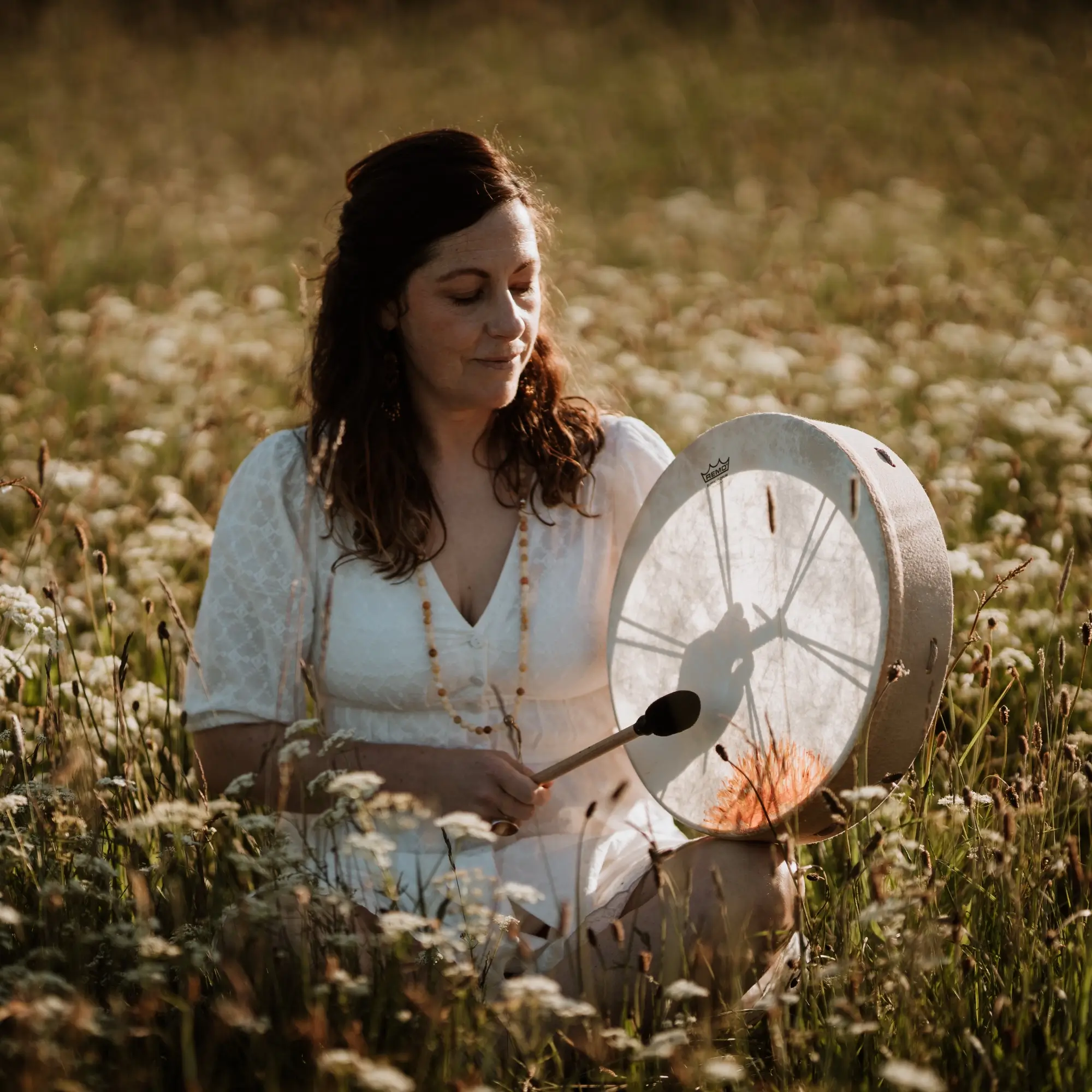 Dawn in white dress sitting in a field of wildflowers playing a drum.