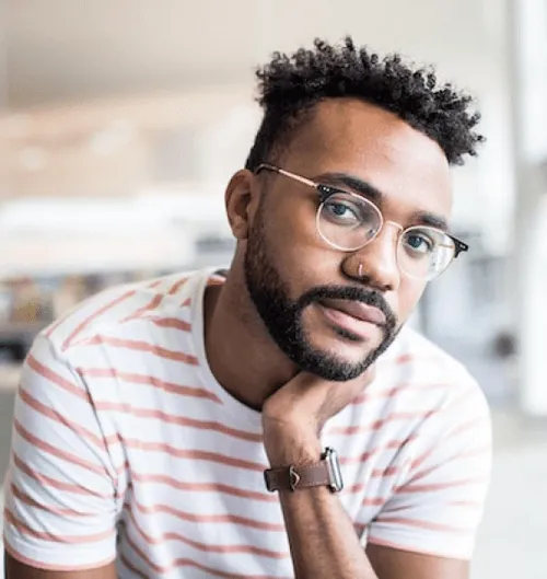 Person wearing a striped shirt and watch, sitting with hand on chin in a bright indoor setting.