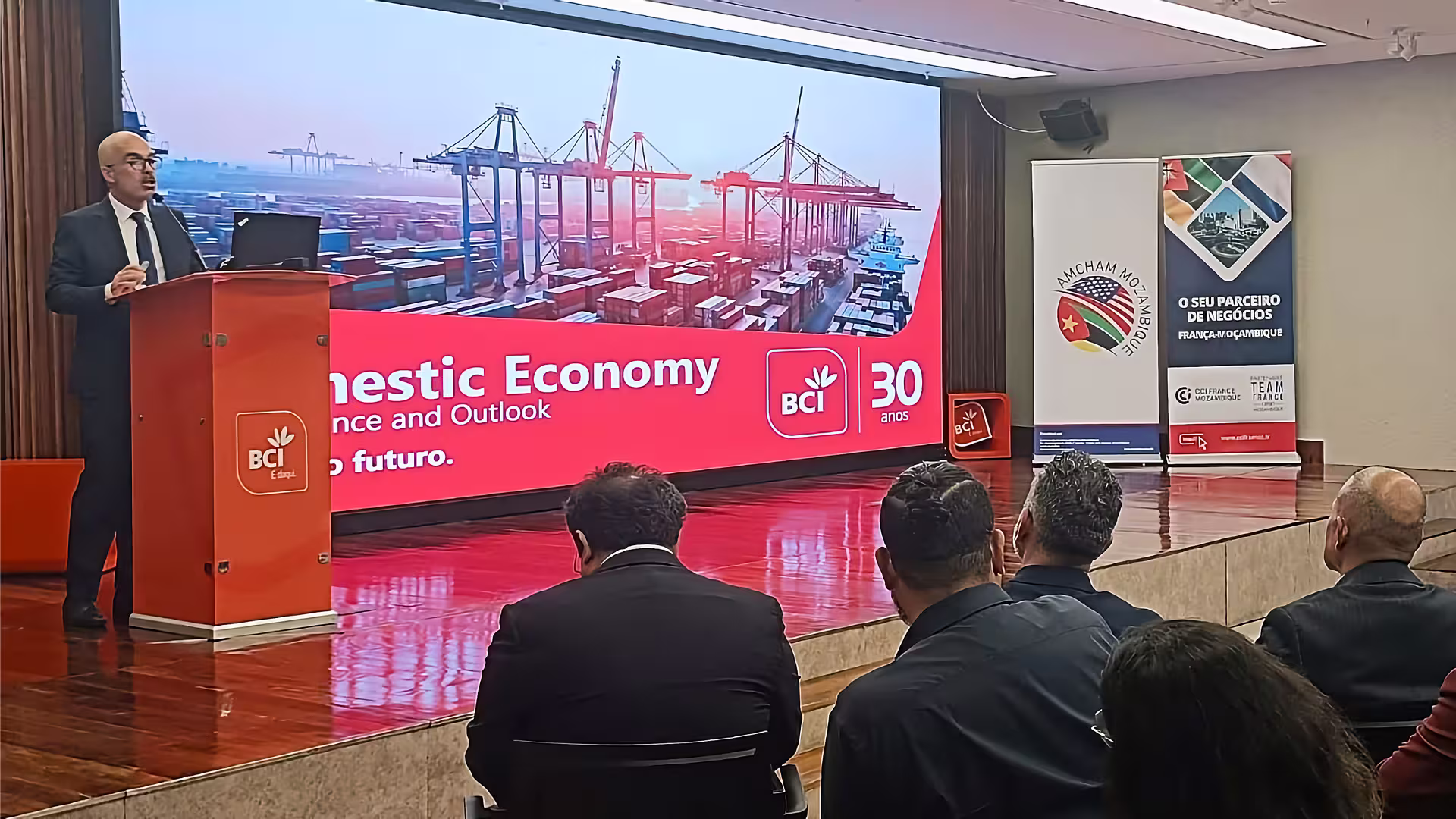 Speaker presenting at the Economic & Business Outlook in Maputo before an audience during an event focused on economic development.