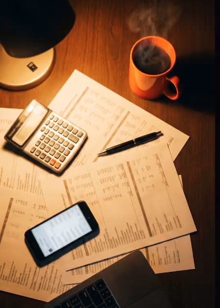 Mesa de trabalho com documentos fiscais, calculadora e café