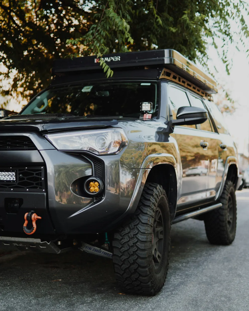 Gray lifted SUV with off-road tires and a rooftop tent parked on a street