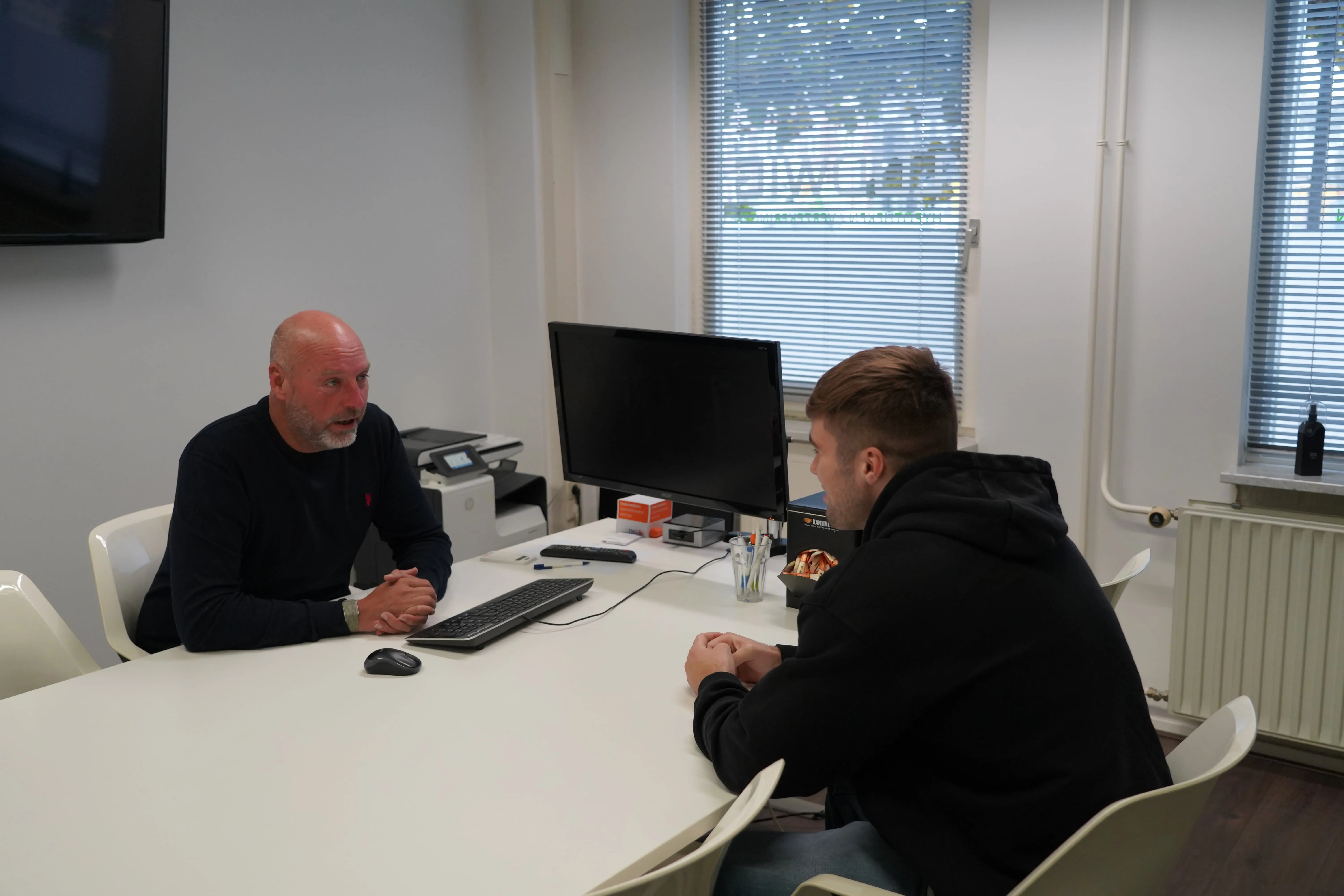 Man en vrouw die aan een bureau zitten en een gesprek voeren in een kantooromgeving.