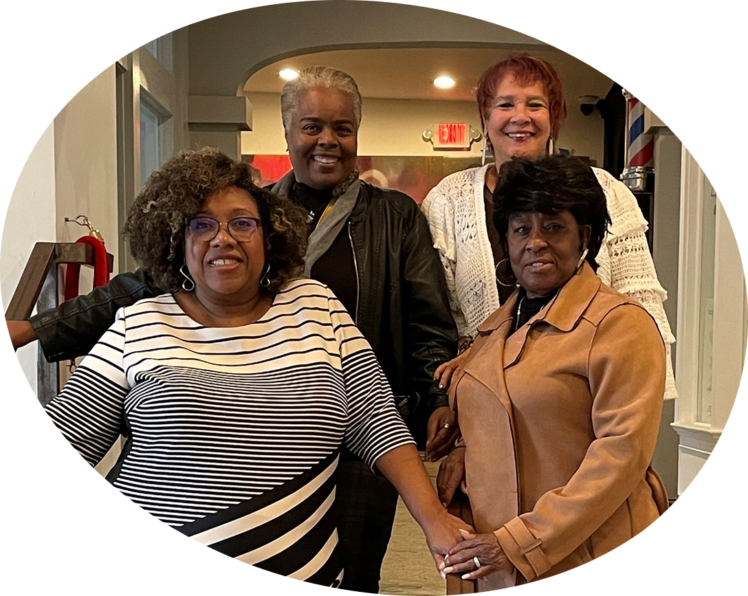 Four smiling women pose together indoors, conveying warmth and friendship. They are dressed stylishly, exuding joy and camaraderie.