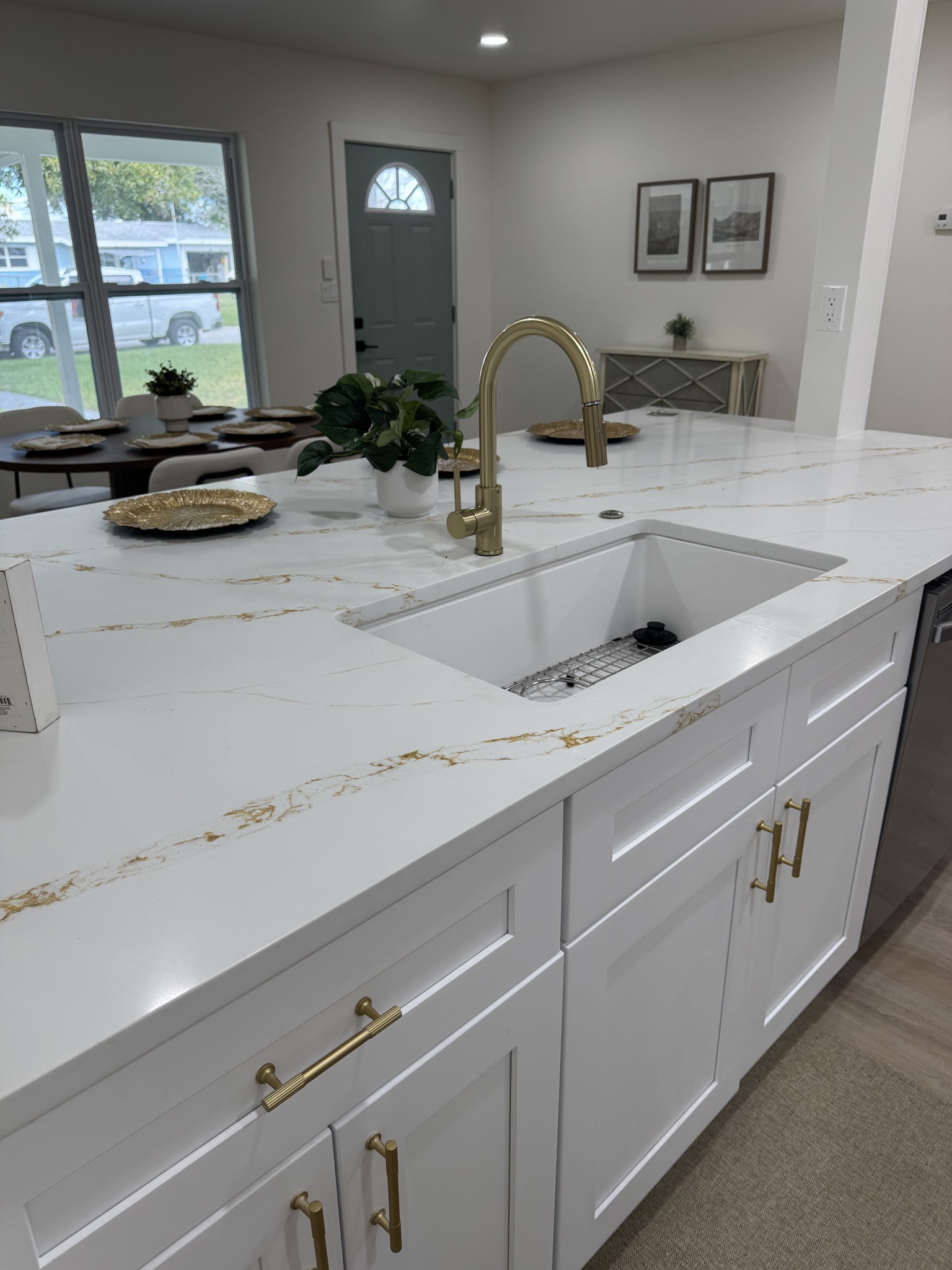 Close-up of a white undermount sink in a quartz countertop with gold veining, paired with a brushed gold pull-down faucet.