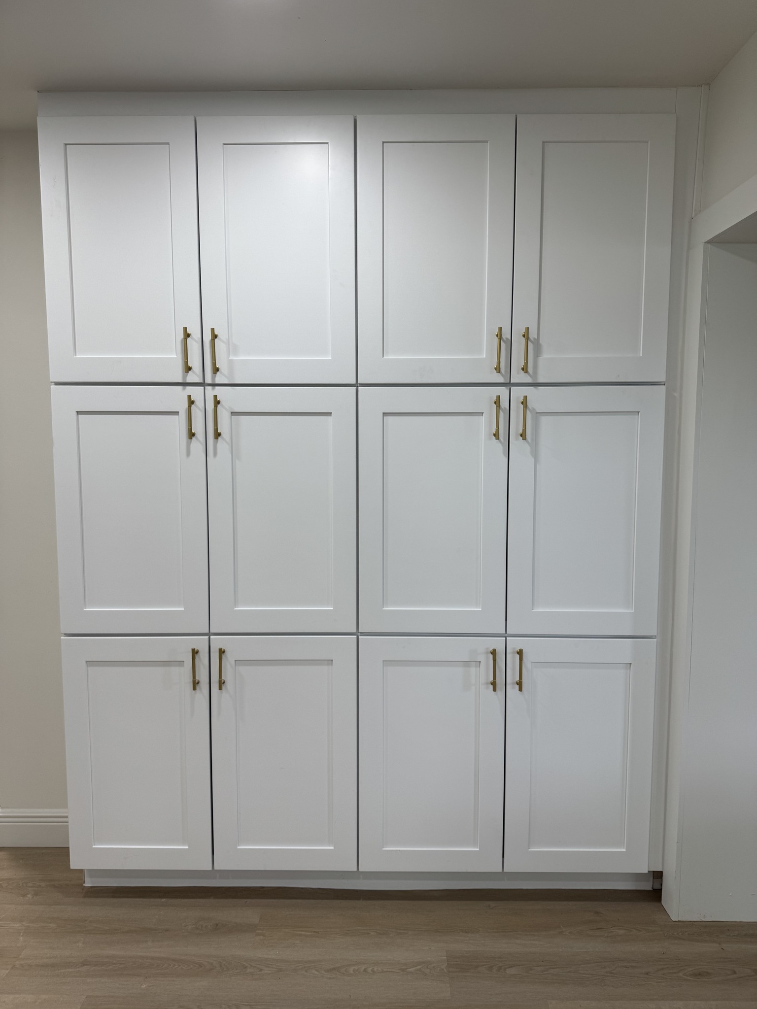 Floor-to-ceiling white shaker-style pantry cabinets with modern gold bar pulls.