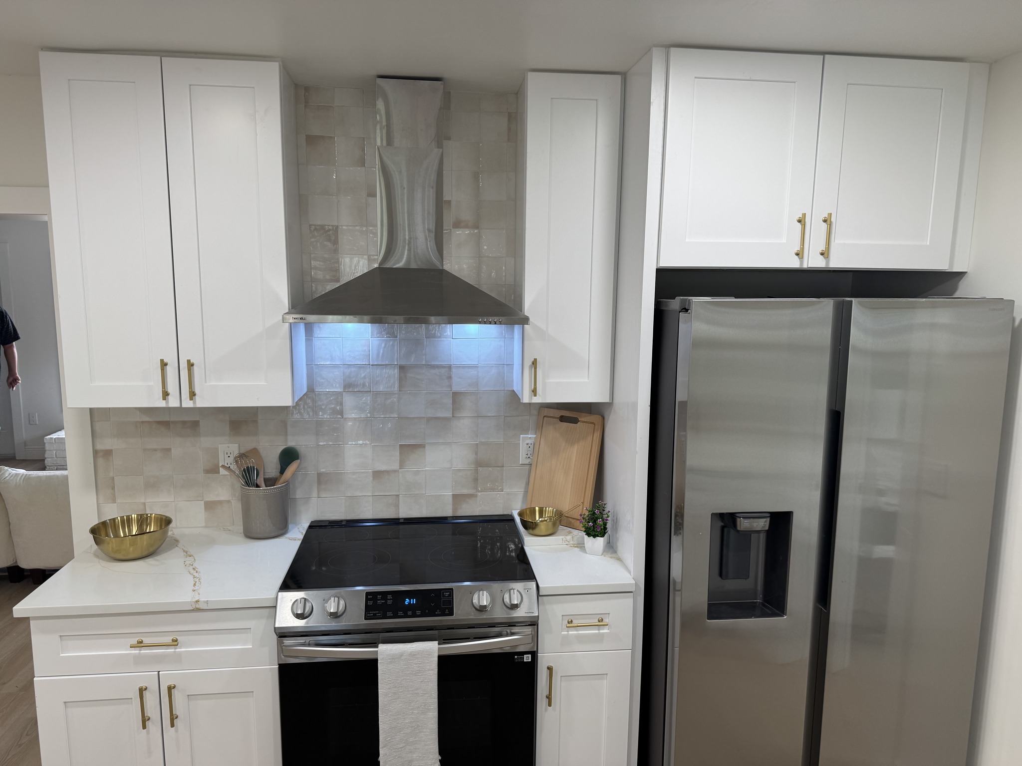 Stainless steel range and hood set against a textured white square tile backsplash with under-cabinet lighting.