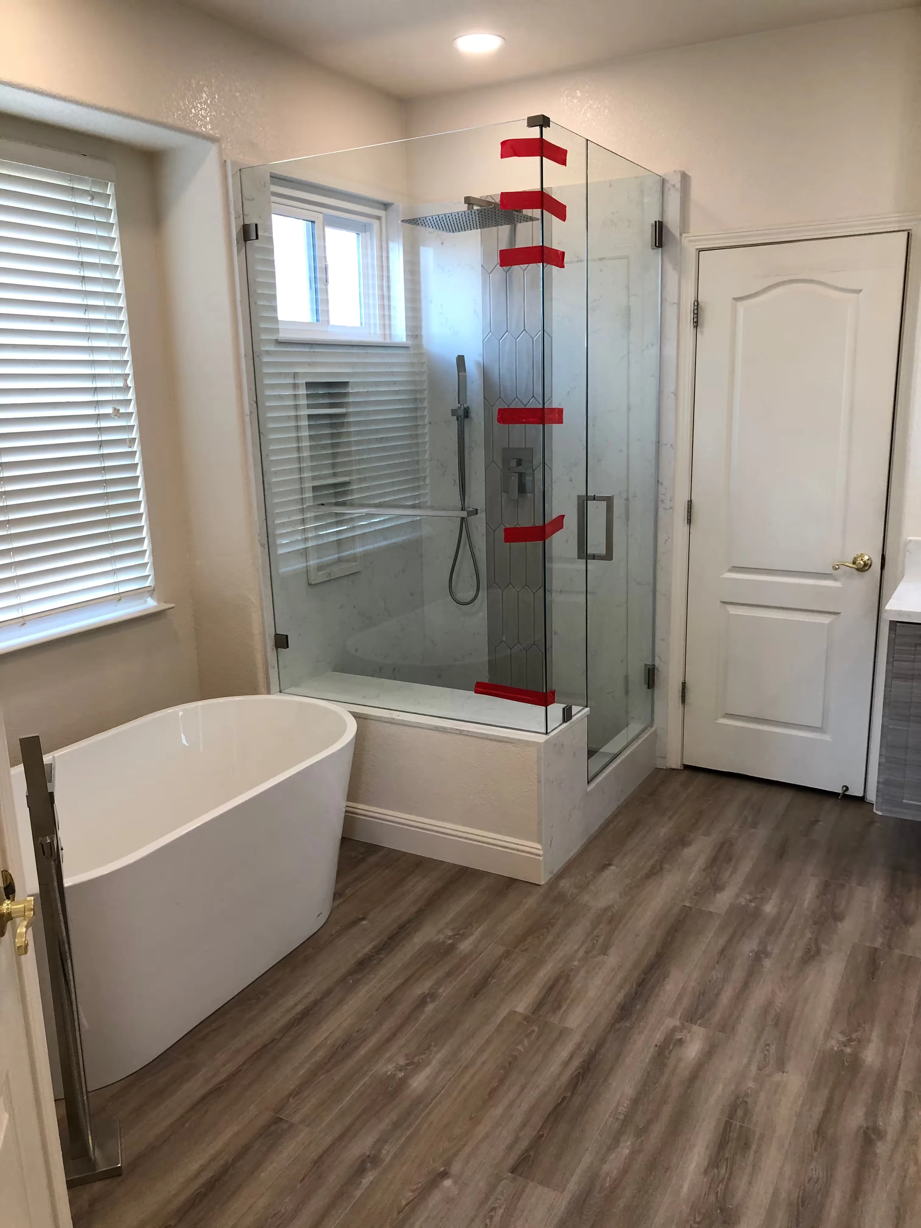 Modern bathroom shower area with gray marble walls, overhead rain shower, and a small gray cabinet with a green plant on top.