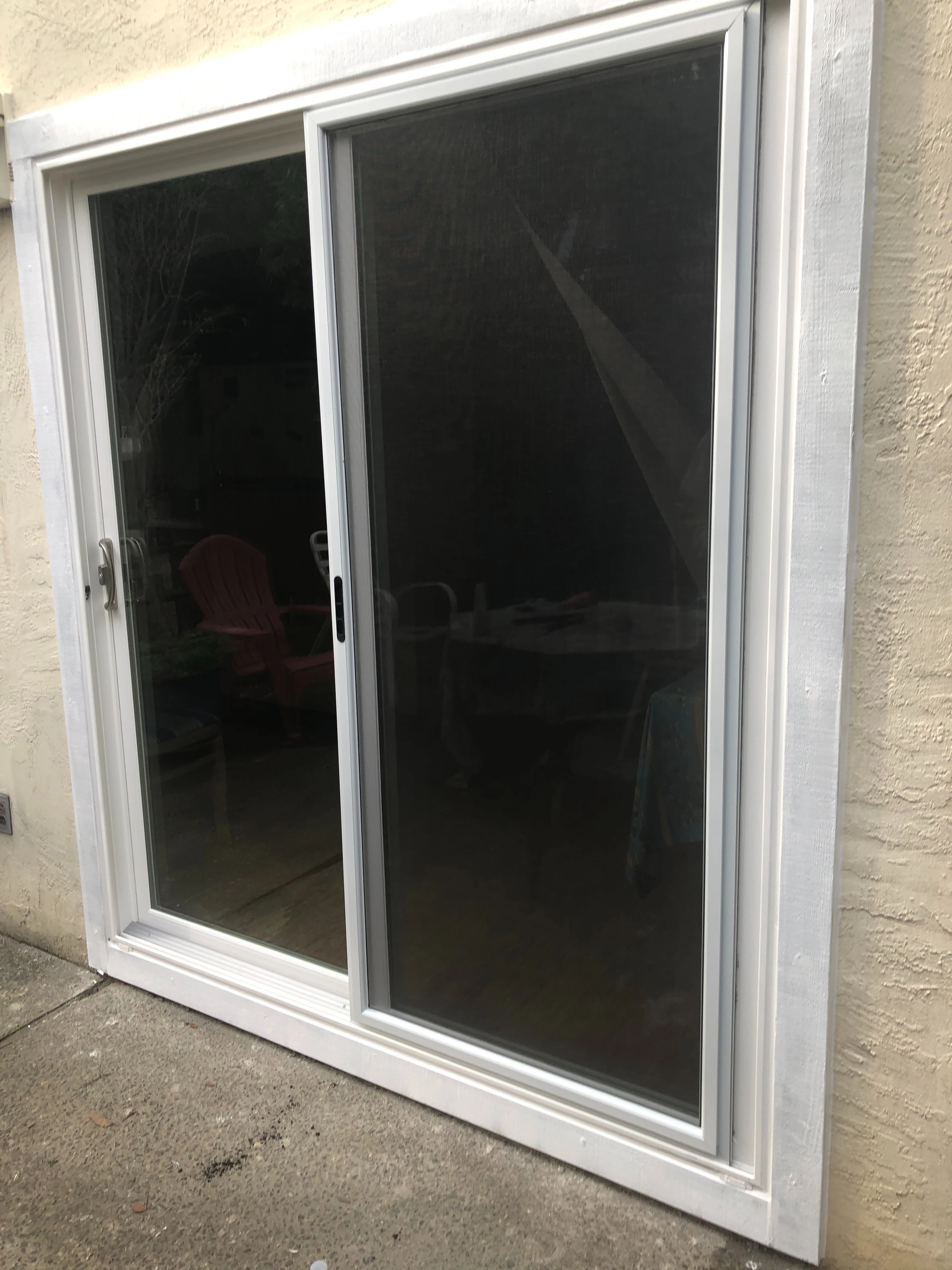 Modern kitchen with light gray cabinetry, white countertops, black fixtures, three wooden stools at island, and a window overlooking greenery.