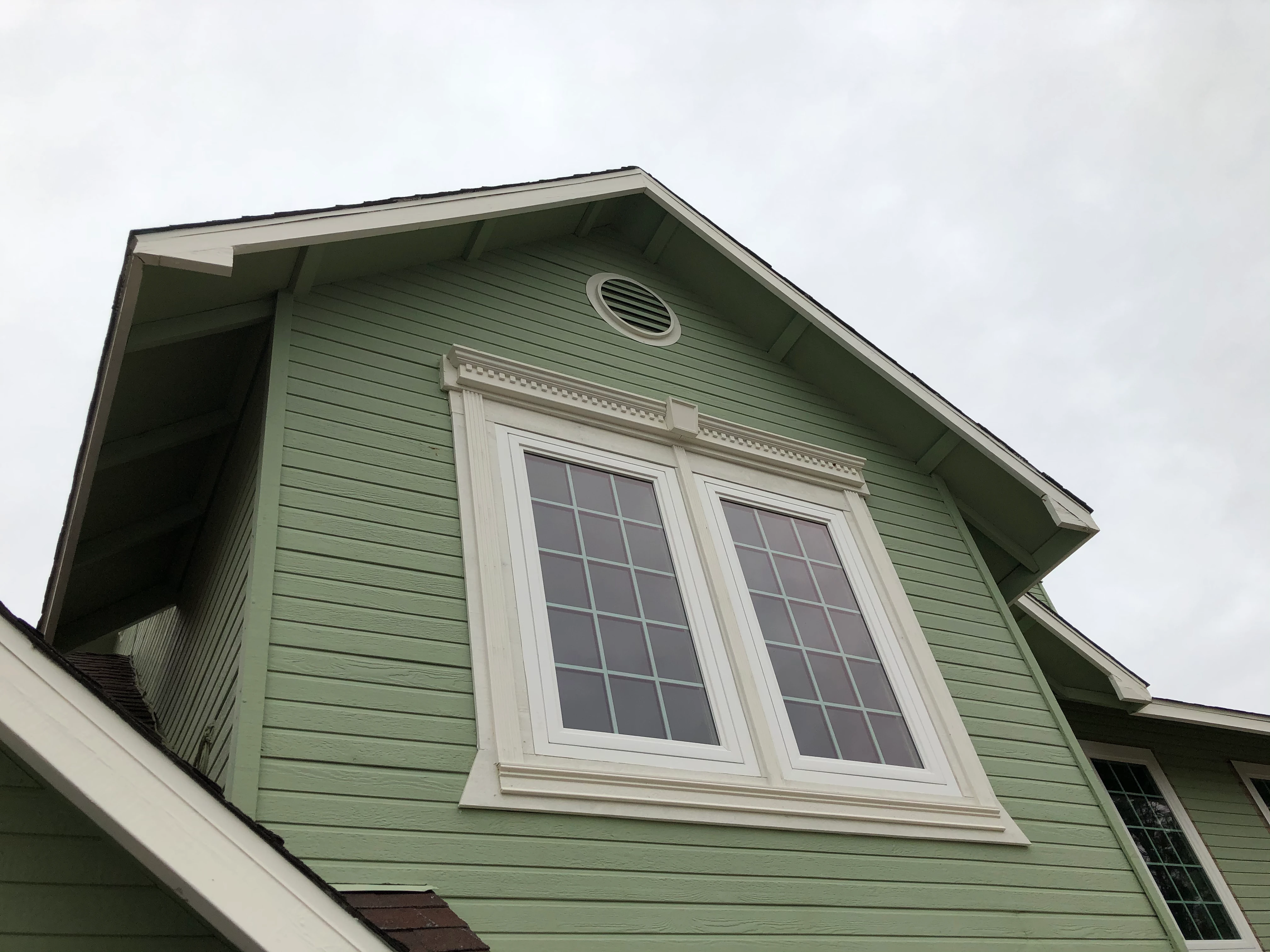 Modern kitchen with light gray cabinetry, white countertops, black fixtures, three wooden stools at island, and a window overlooking greenery.