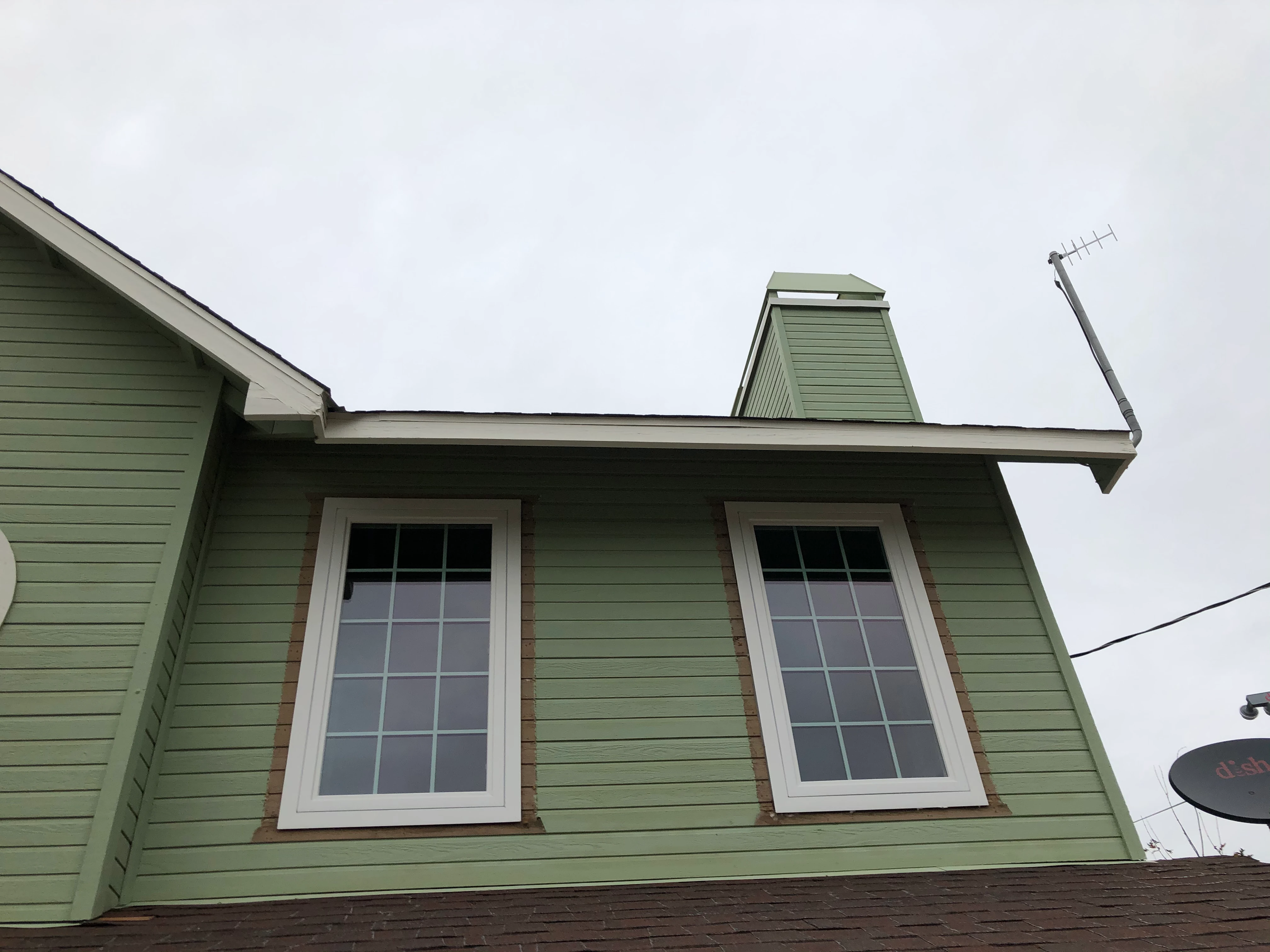 Modern kitchen with light gray cabinetry, white countertops, black fixtures, three wooden stools at island, and a window overlooking greenery.