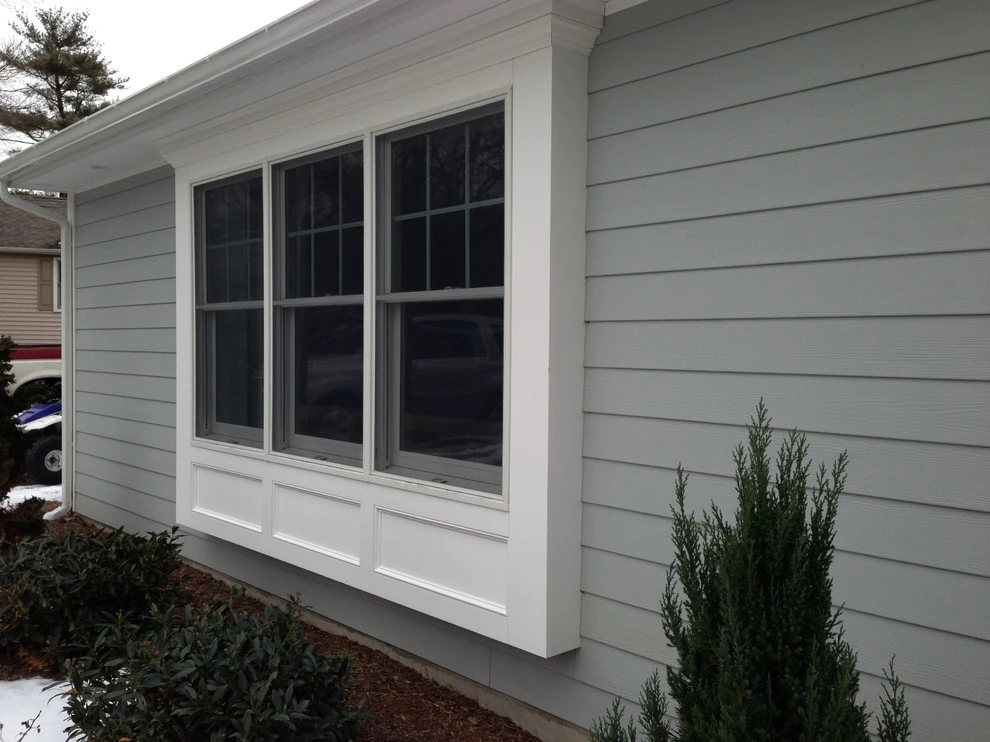 Modern kitchen with light gray cabinetry, white countertops, black fixtures, three wooden stools at island, and a window overlooking greenery.