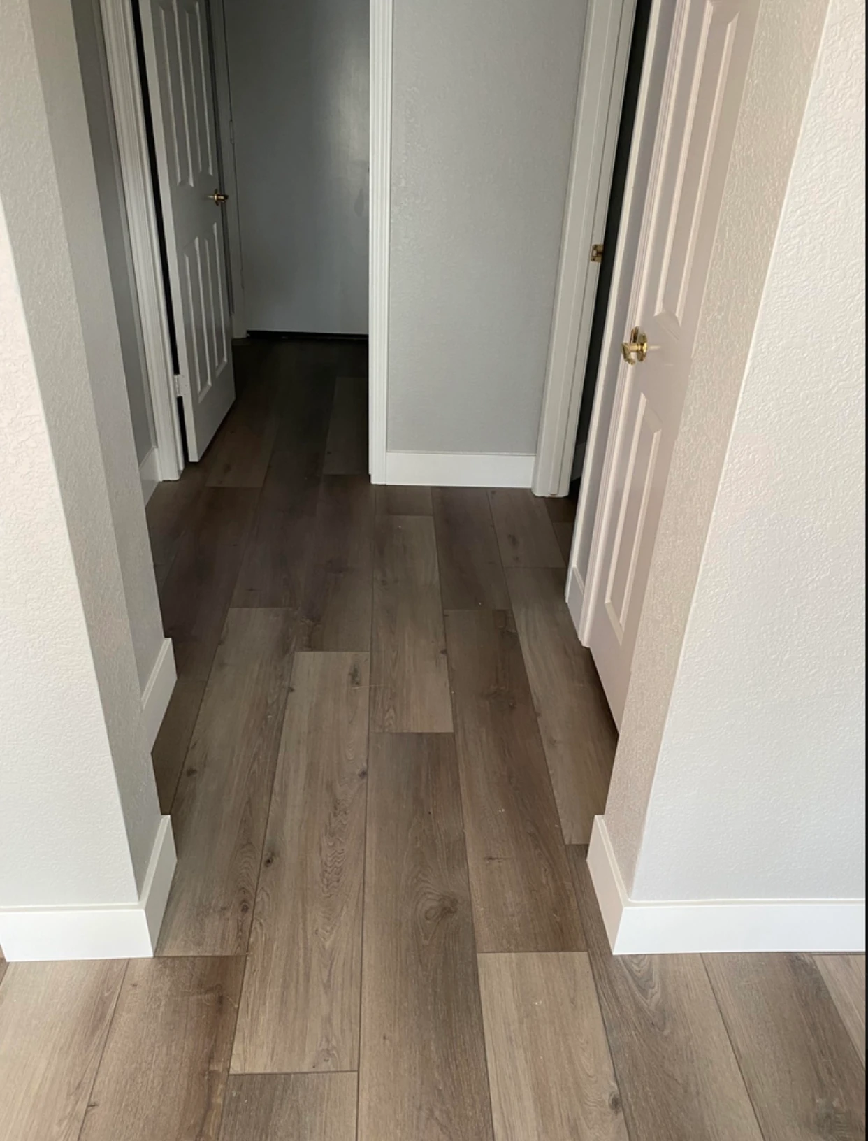 Modern kitchen with light gray cabinetry, white countertops, black fixtures, three wooden stools at island, and a window overlooking greenery.