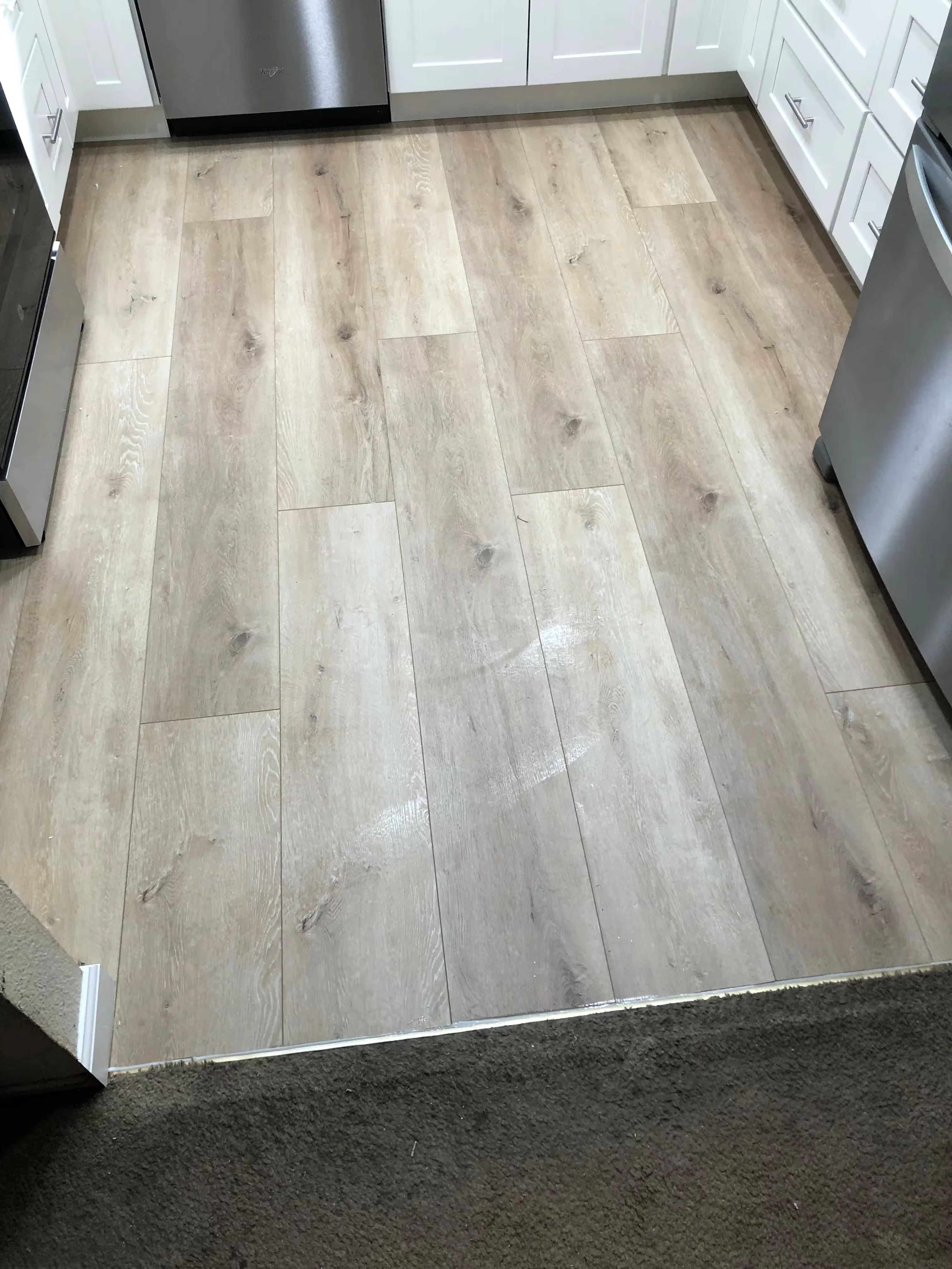 Modern kitchen with light gray cabinetry, white countertops, black fixtures, three wooden stools at island, and a window overlooking greenery.