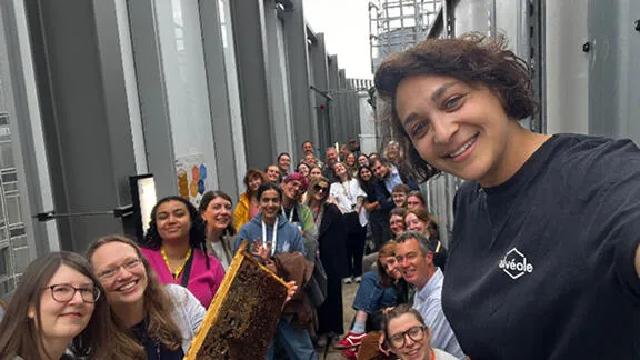 Alvéole beekeeper taking a group selfie with a large smiling crowd on a rooftop, honeycomb frame in hand