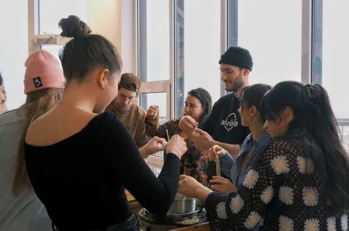 Group of young people gathered around an Alvéole instructor at an indoor demo and workshop, handling honeycomb and beekeeping materials
