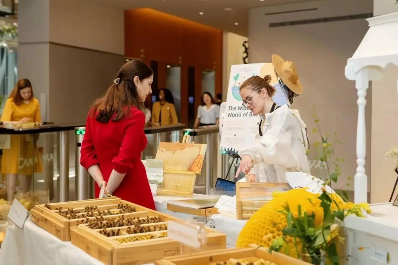 Alvéole educator at an elegant indoor activation booth with honeycomb displays, beekeeping boxes, and floral arrangements, asset managers reporting