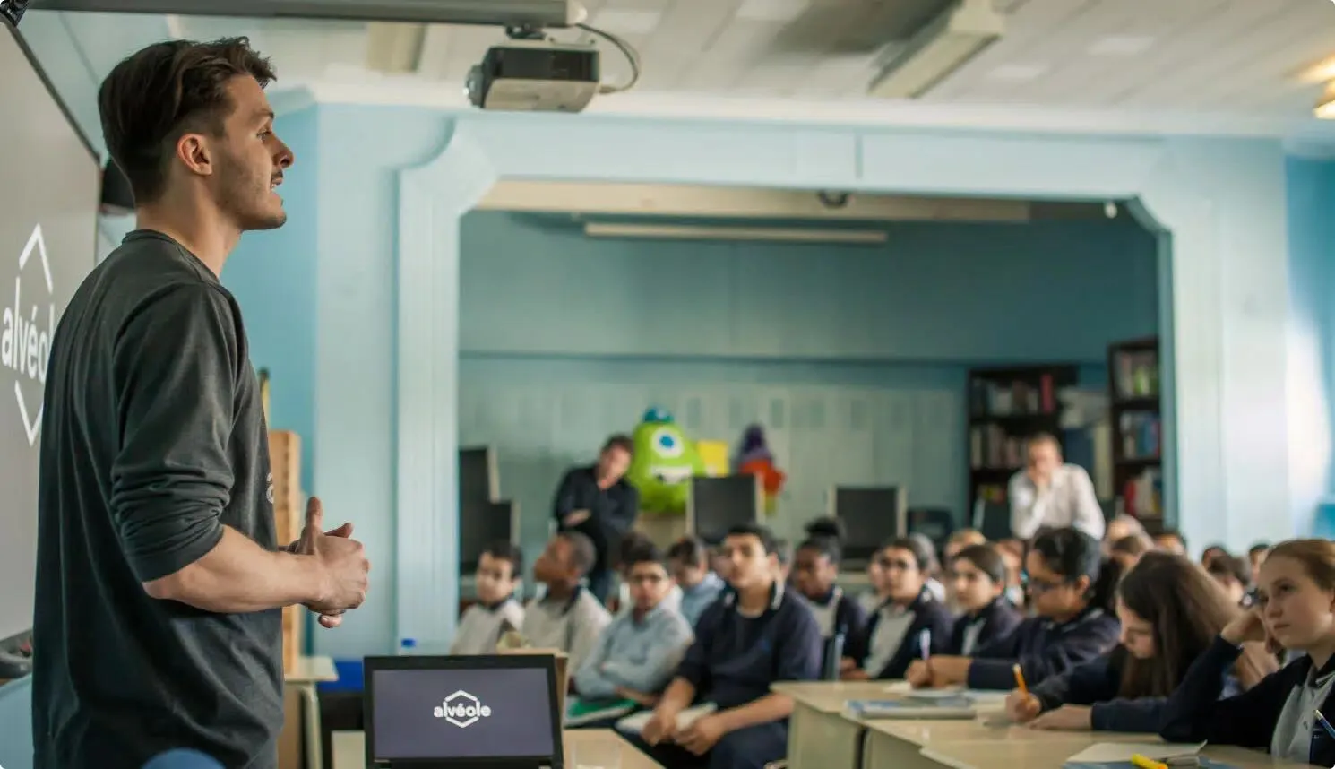 Alvéole educator presenting to a large classroom of attentive students with a laptop showing the Alvéole logo at the front