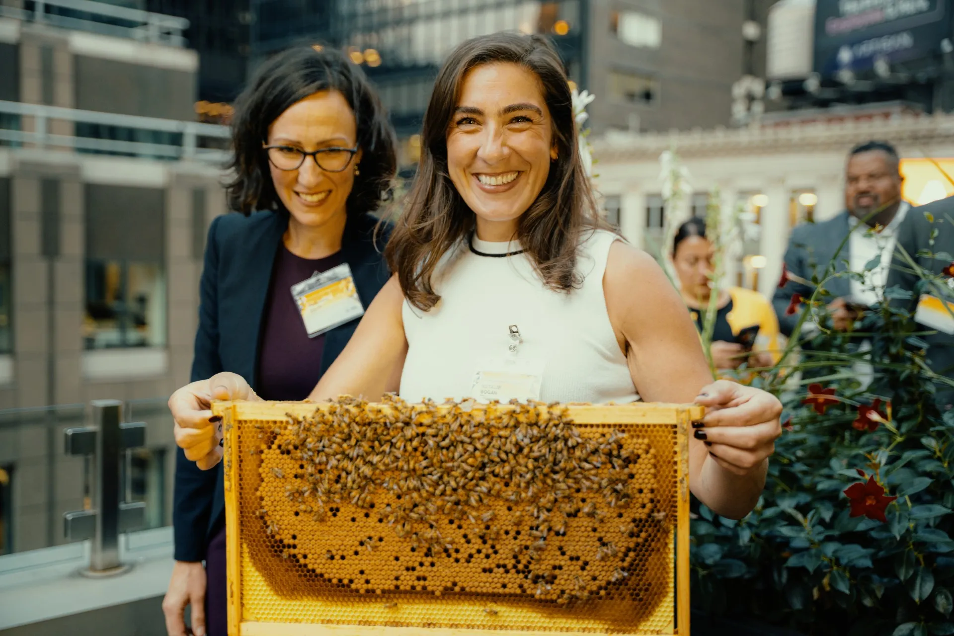 Smiling woman proudly holding a large honeycomb frame covered in bees at an Alvéole rooftop beekeeping workshop at a hotel venue