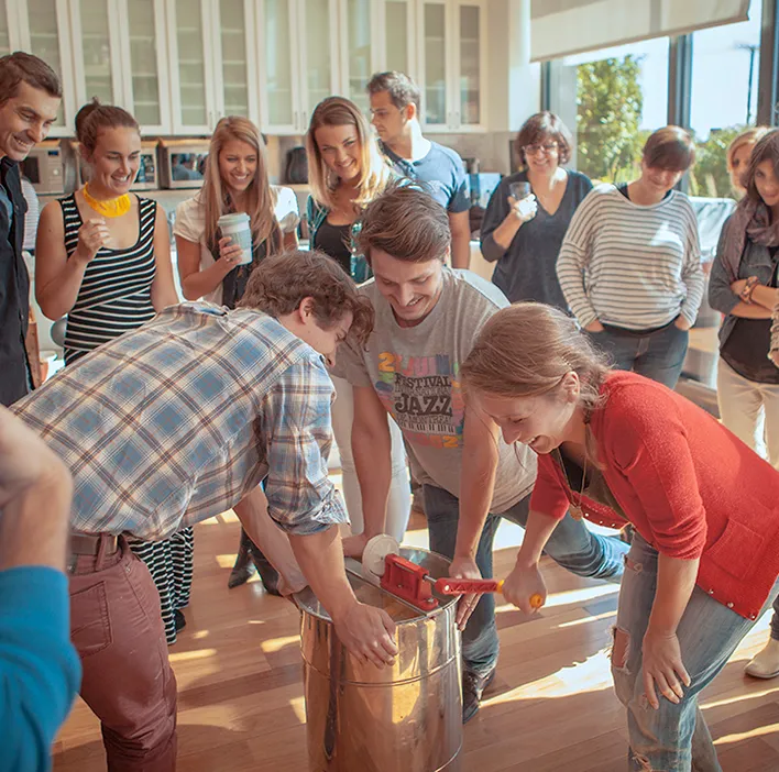 Group of employees laughing together around a hand-crank honey extractor during an Alvéole From Hive to Honey Jar workshop