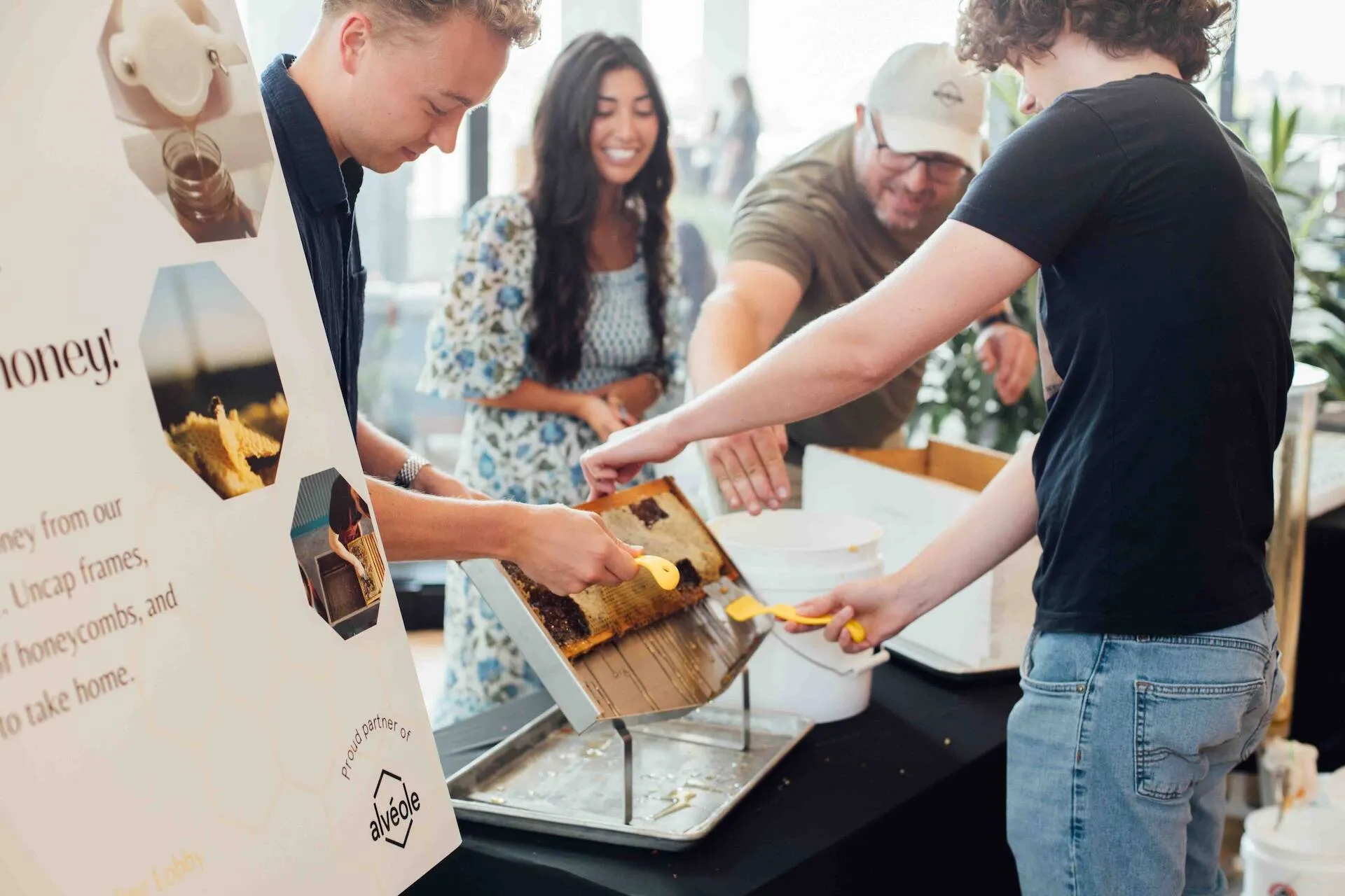 Participants uncapping honeycomb frames and extracting honey at an indoor Alvéole honey harvesting event
