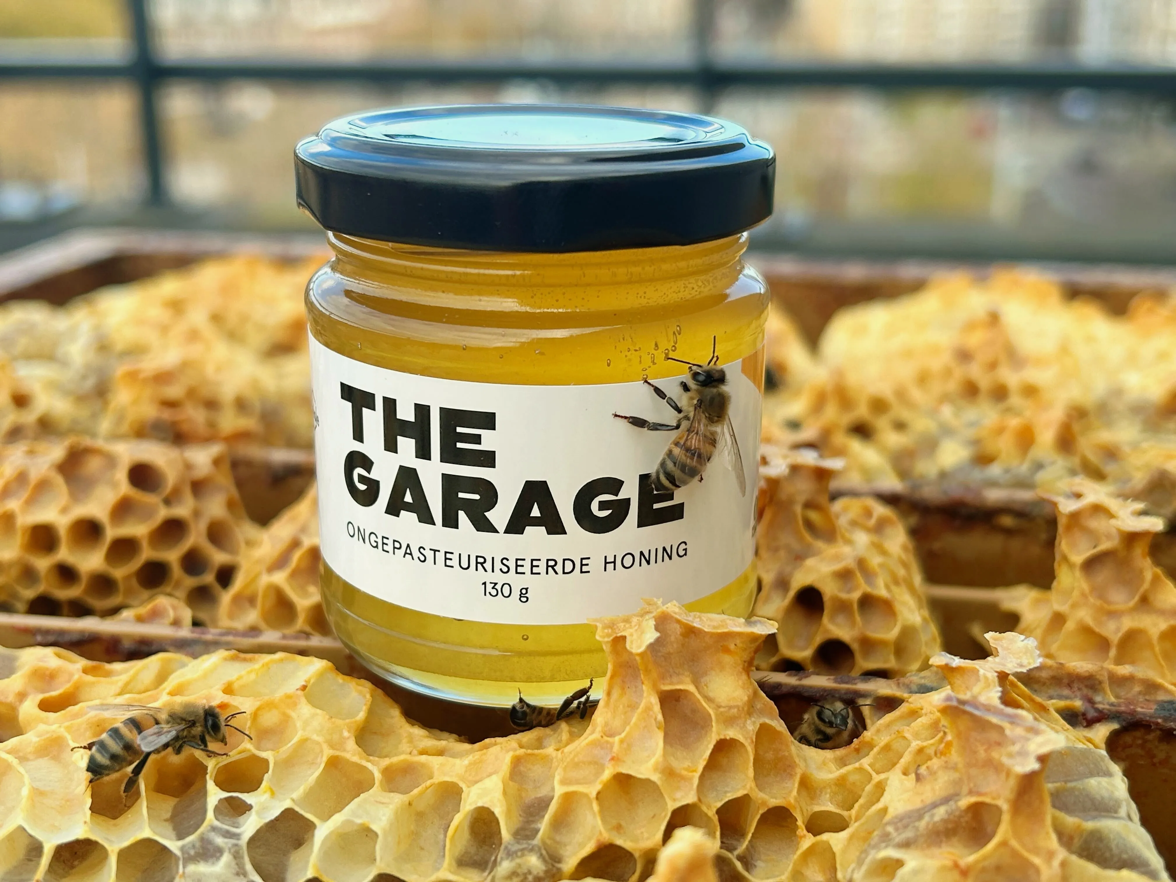 A custom-branded honey jar for The Garage sitting on golden honeycomb with bees nearby