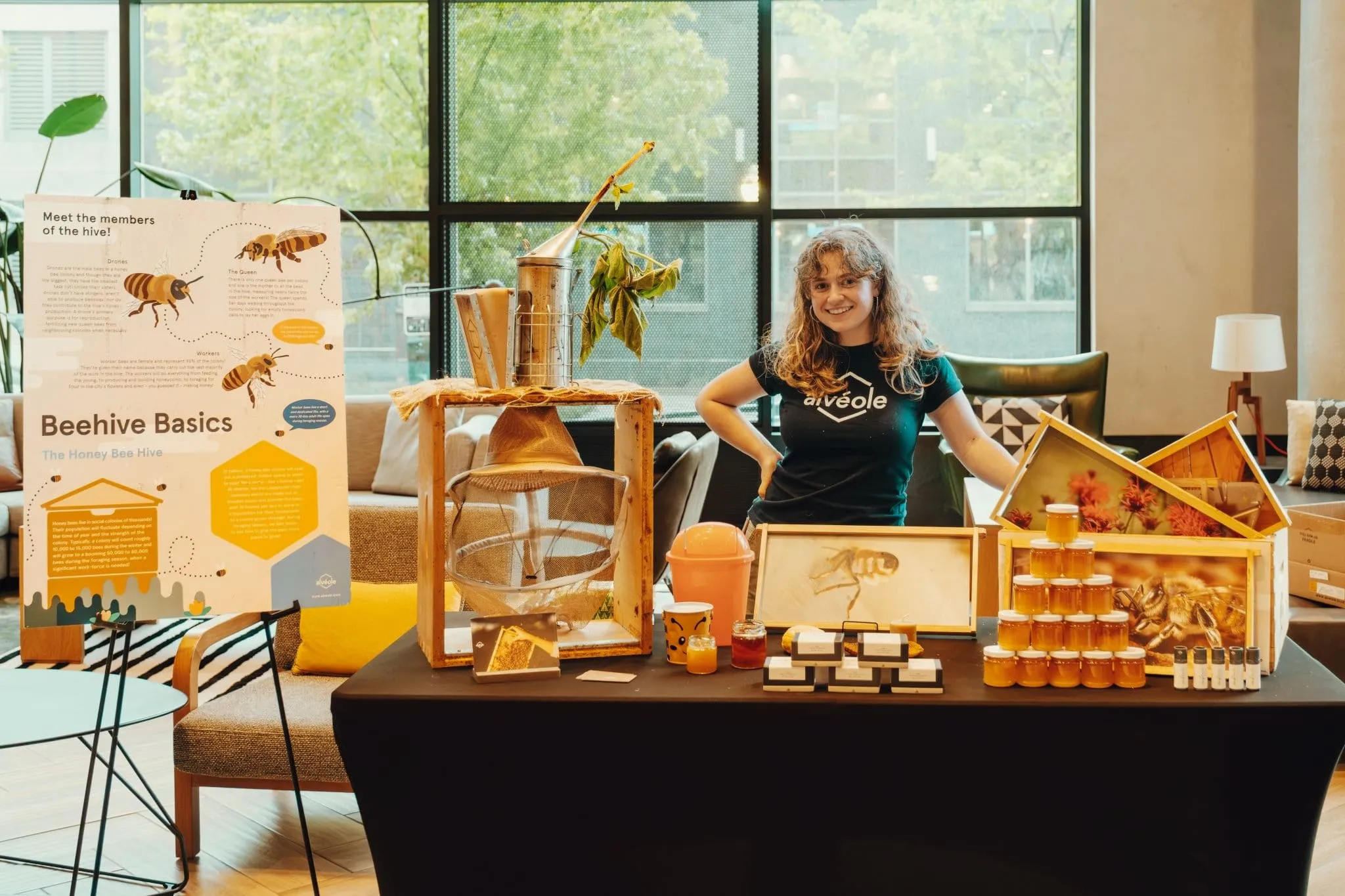 An Alveole team member standing behind a beekeeping education booth with honey jars and a beehive basics display