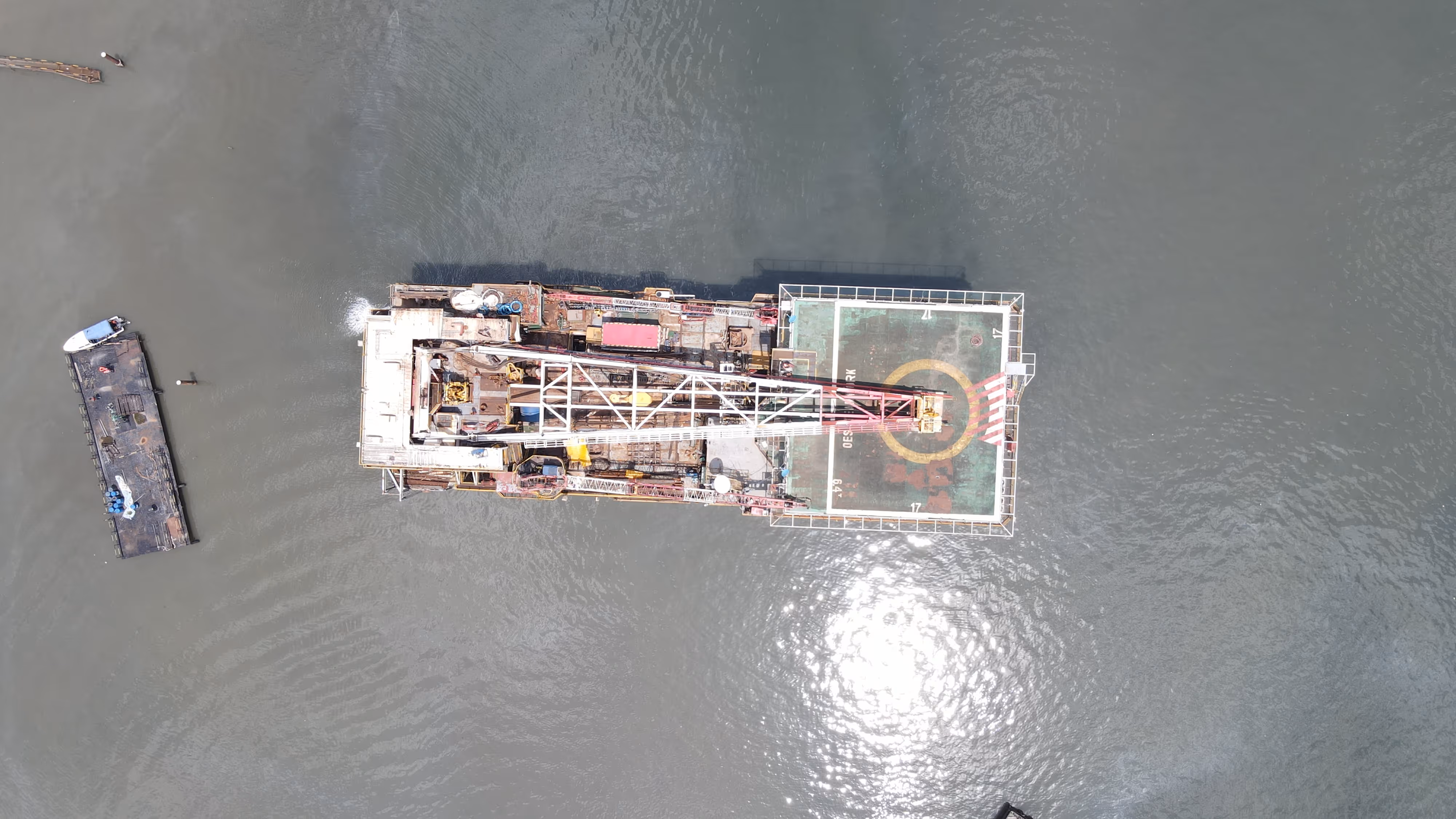 Aerial view of an industrial barge with a crane and a helipad on a body of water.