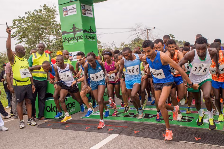 Runners starting a 10km road race at the Okpekpe race starting line, with an official holding a starter pistol raised.