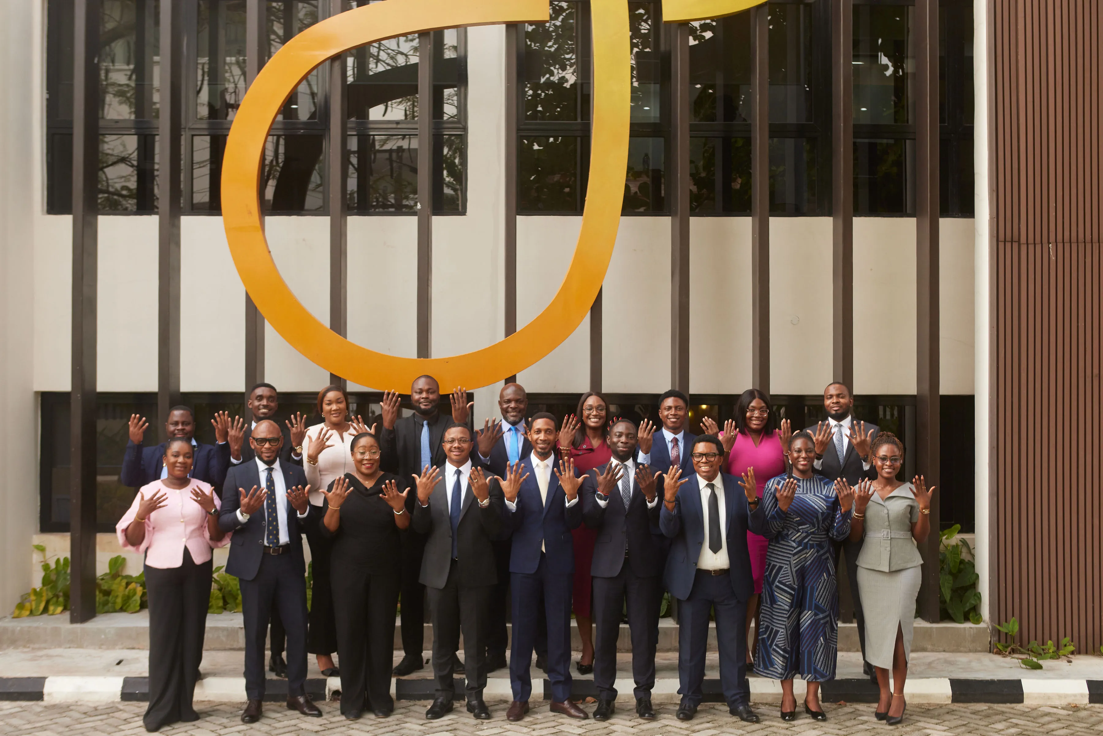 Group of diverse professionals in business attire standing outdoors, smiling and holding up their hands displaying rings.
