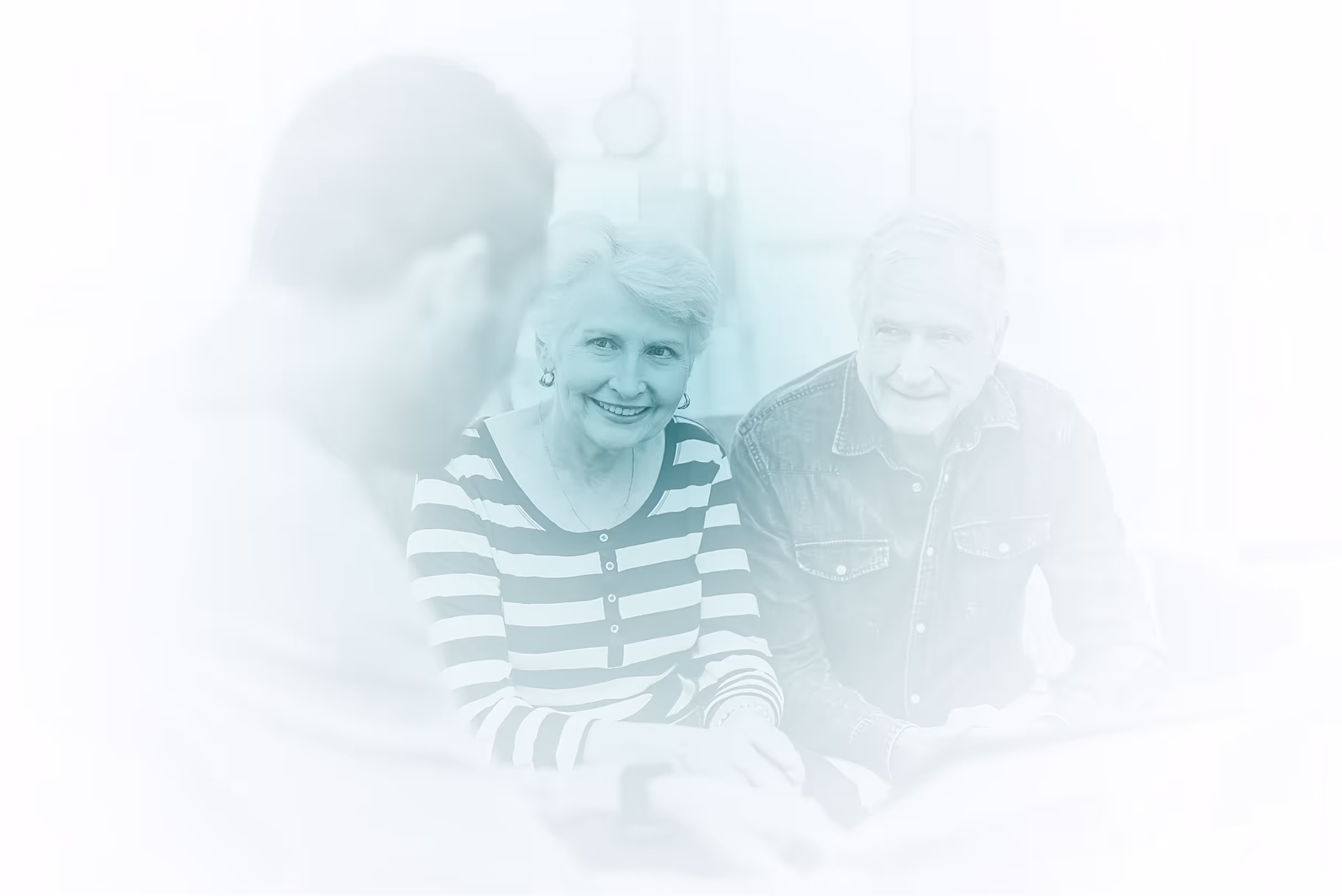 Smiling elderly couple sitting and talking to a younger man in a bright room.