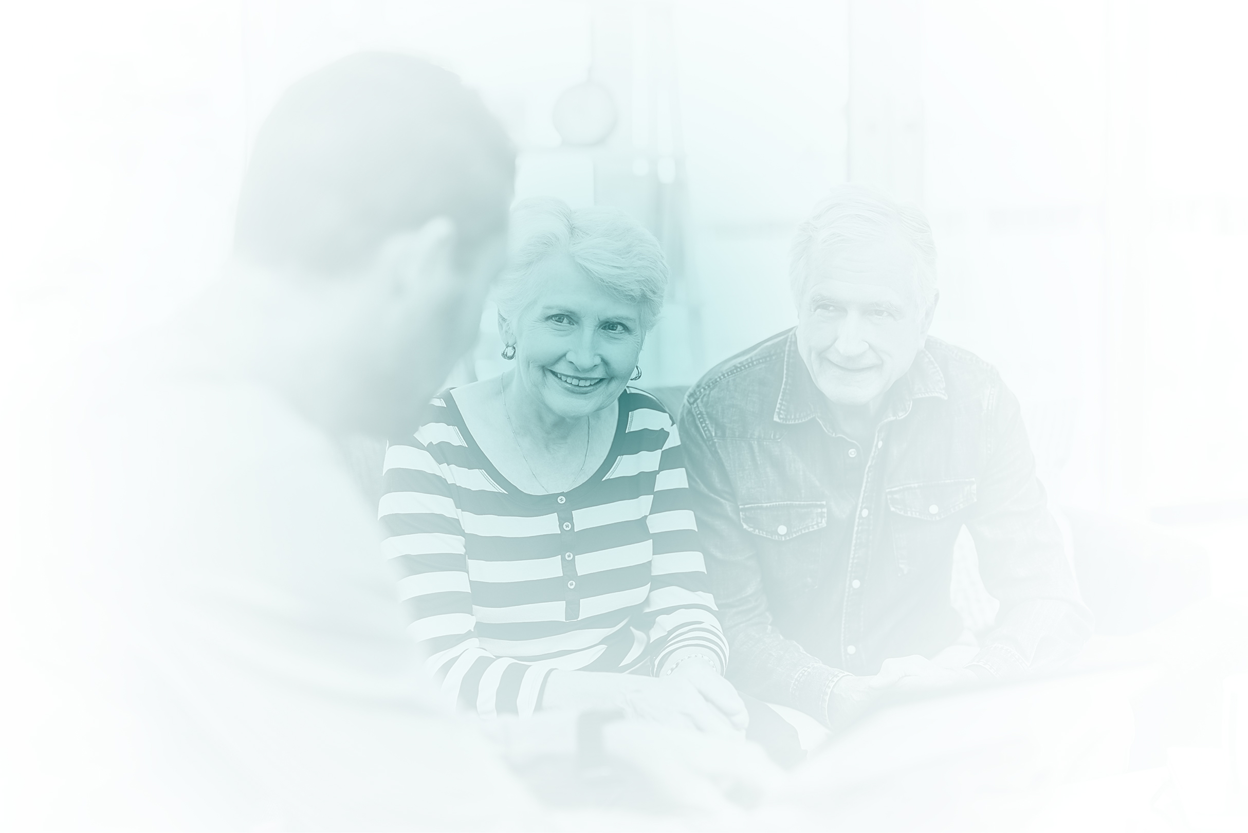 Smiling elderly couple sitting and talking to a younger man in a bright room.