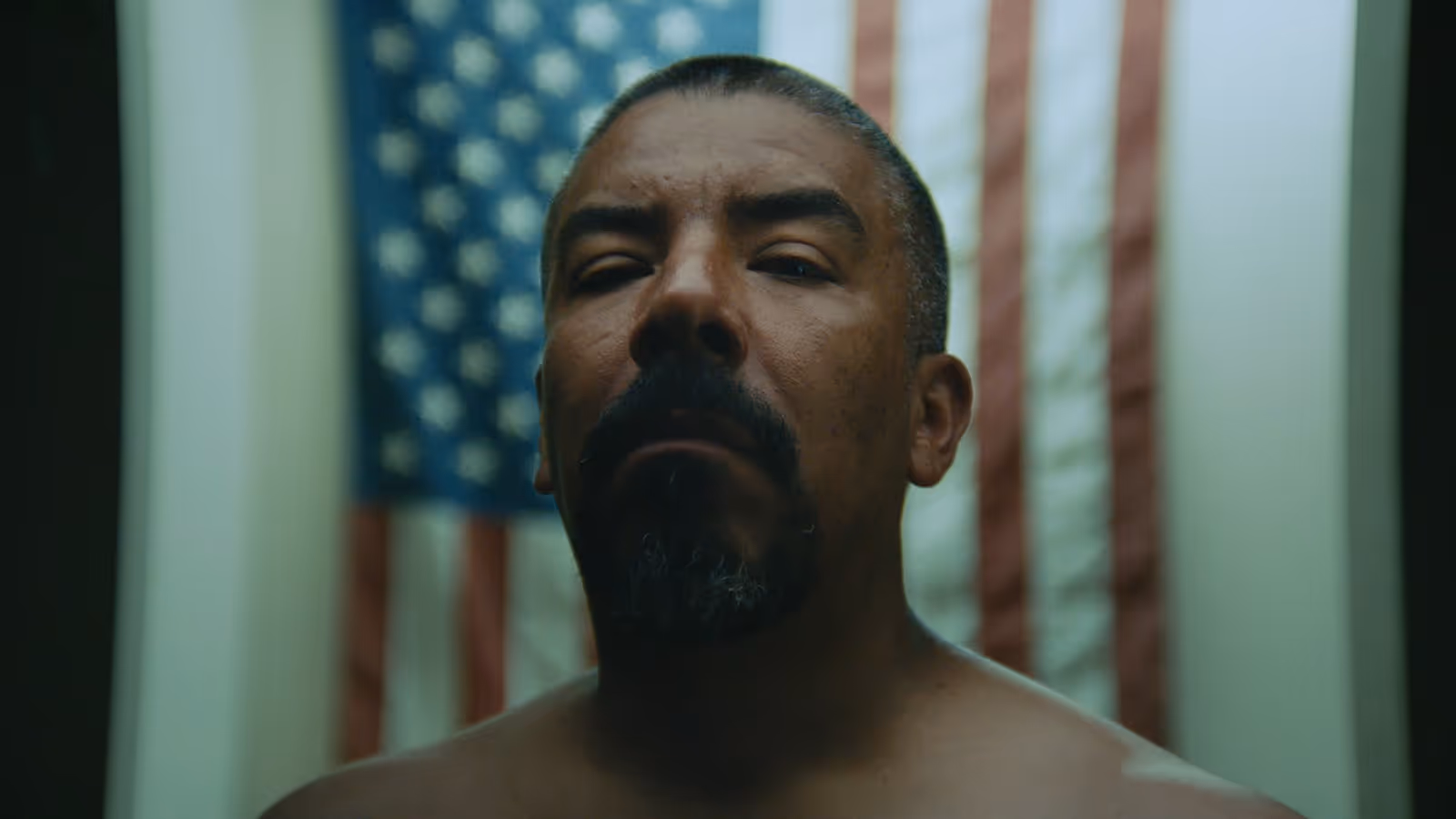 Dramatic close-up of a Mexican-American man standing in front of an American flag.