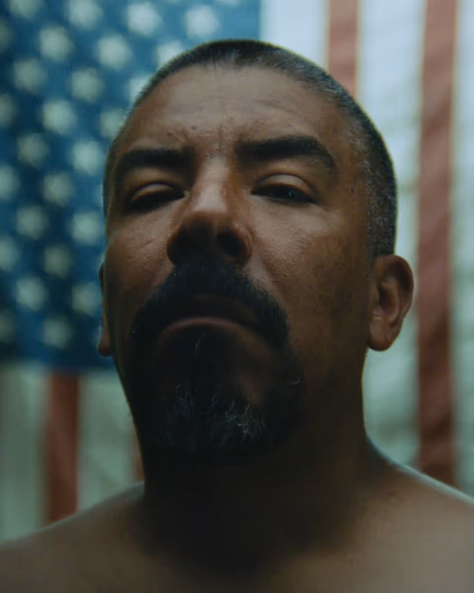 Dramatic close-up of a Mexican-American man standing in front of an American flag.