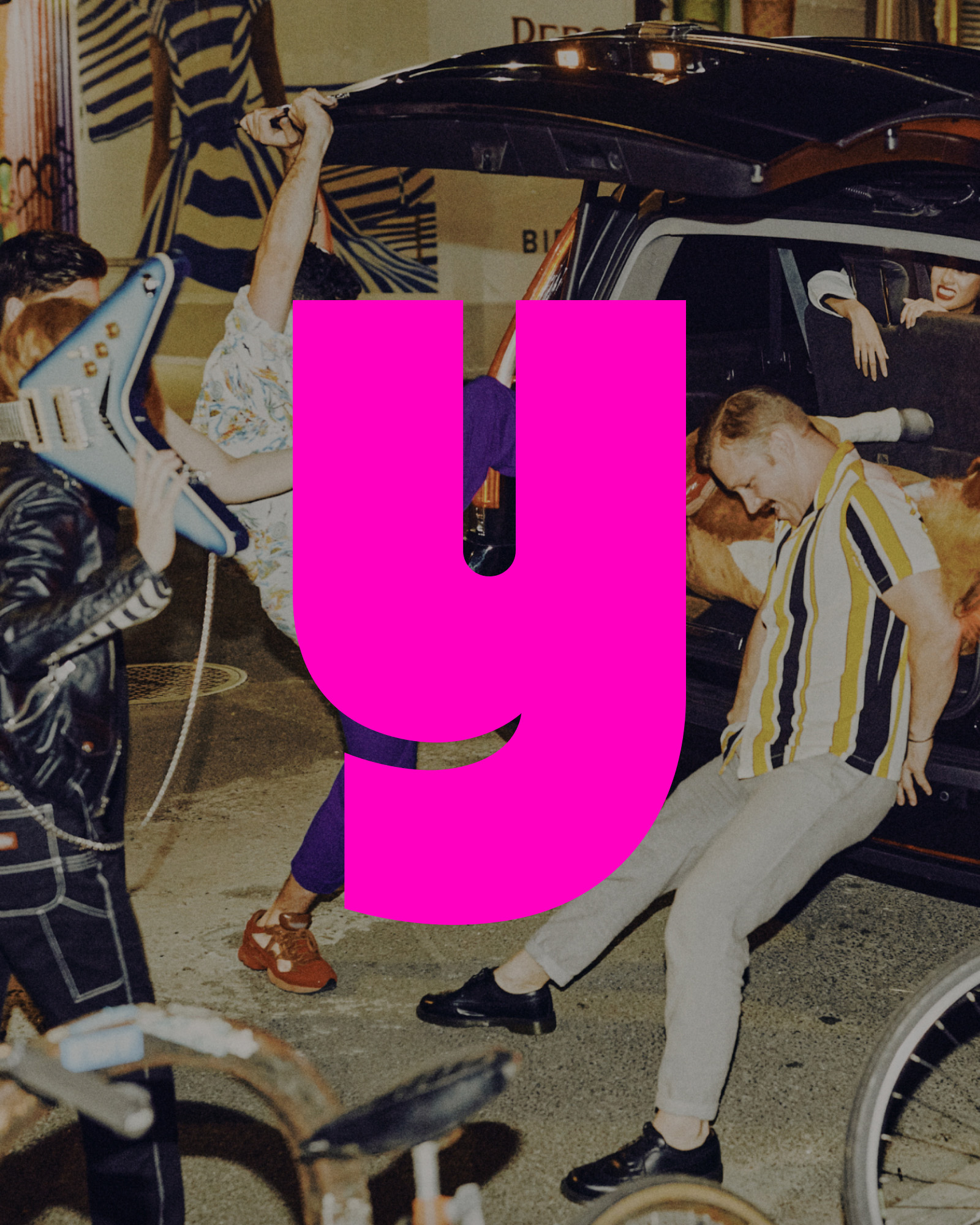 Behind-the-scenes photo shoot with people filling the trunk of a black SUV with music equipment and a stuffed horse on urban street at night