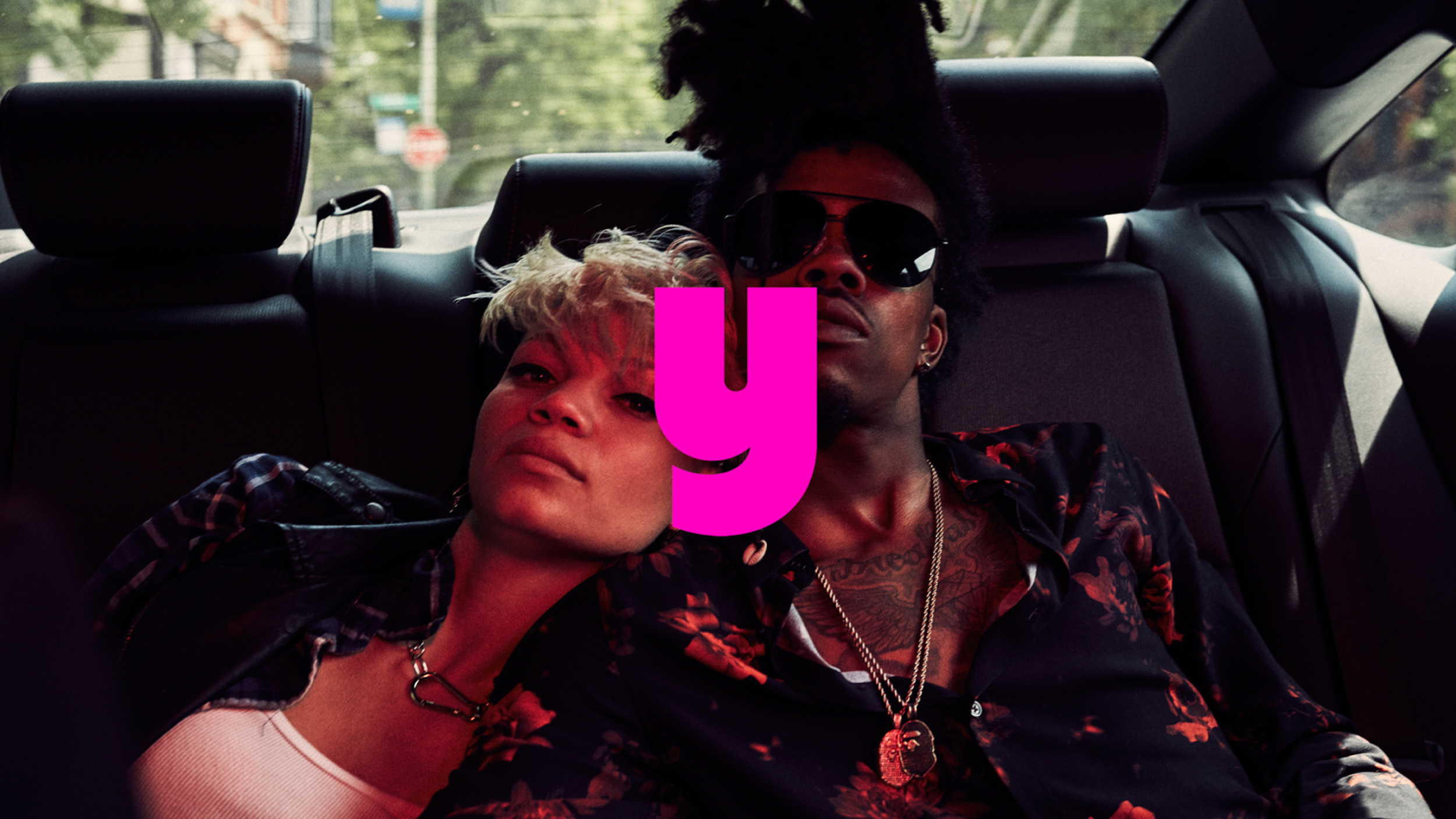 Behind-the-scenes photo shoot with people filling the trunk of a black SUV with music equipment and a stuffed horse on urban street at night