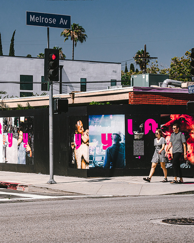 Street corner with a wall of pink Lyft Y wildposting posters and a passerby