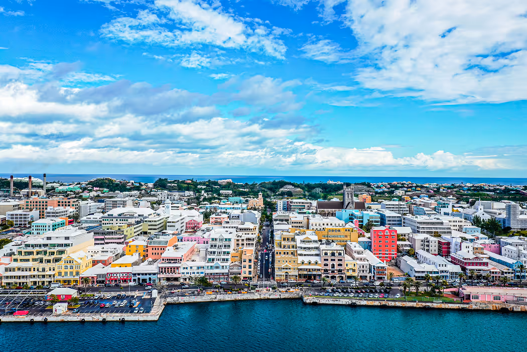 Aerial view of a colorful coastal city with pastel buildings, a waterfront, and blue sky with scattered clouds.